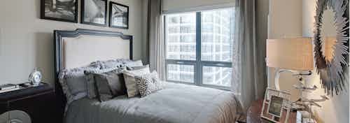 Elegant bedroom at AMLI River North with a large grey bed in front of a window with flowing curtains and a daytime city view
