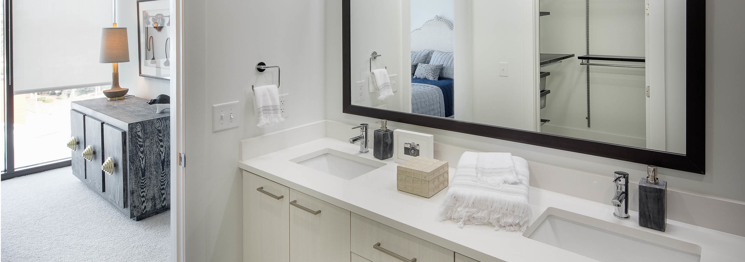 Interior of bathroom at AMLI 3464 with double vanity sink and white cabinets with open door leading to bedroom