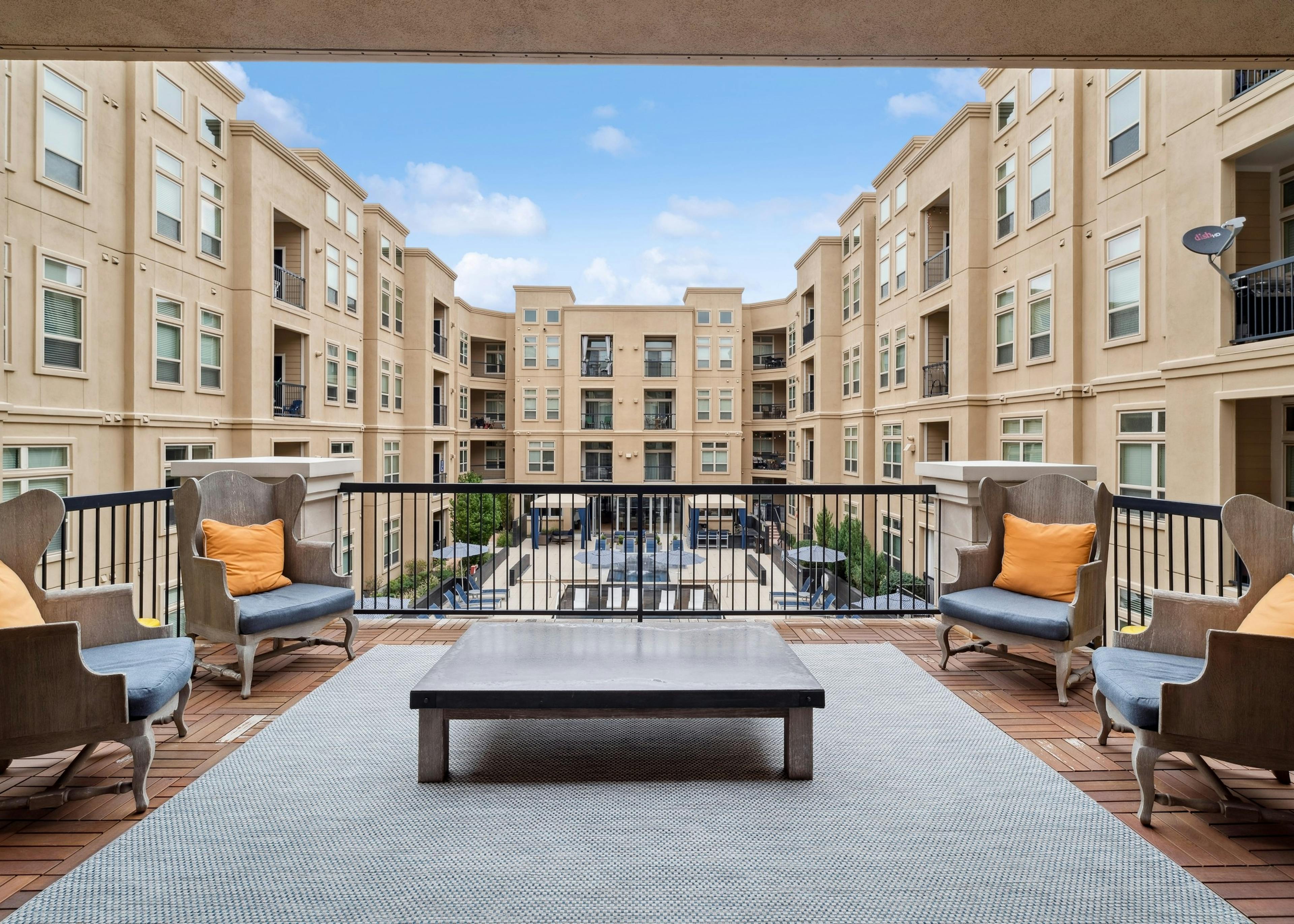 Exterior view of a library outdoor lounge at AMLI RidgeGate with chairs and area rug and table and a view of the pool area