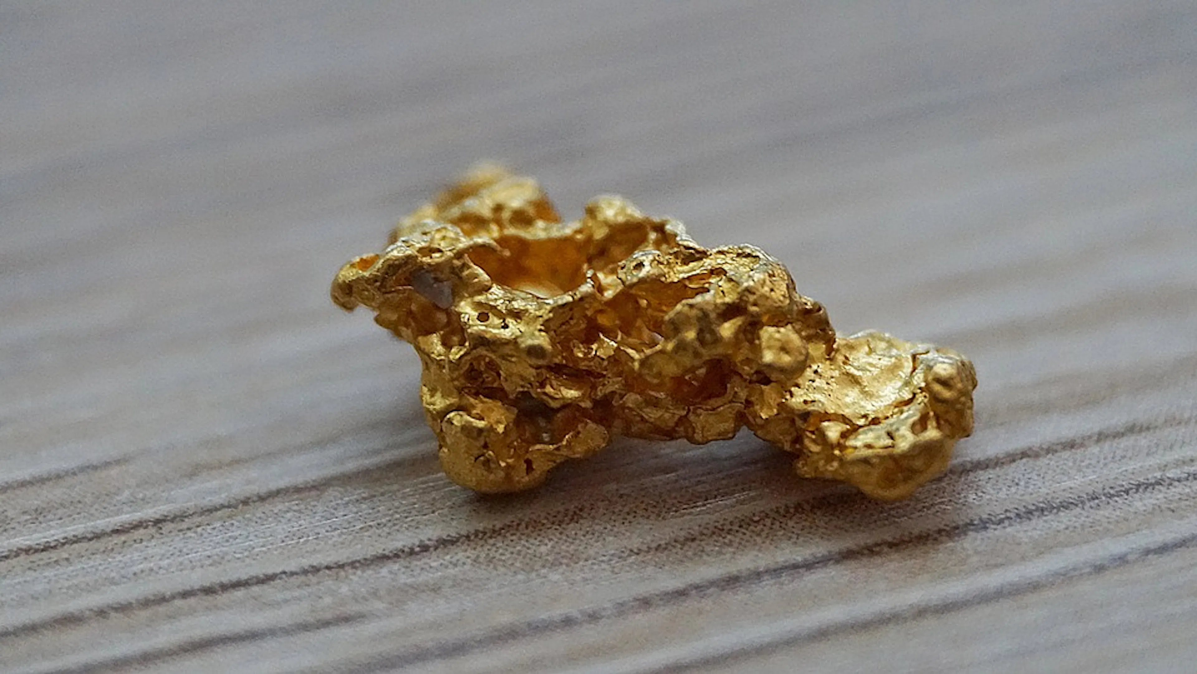 A gold nugget roughly the size of an almond resting on a wooden bench