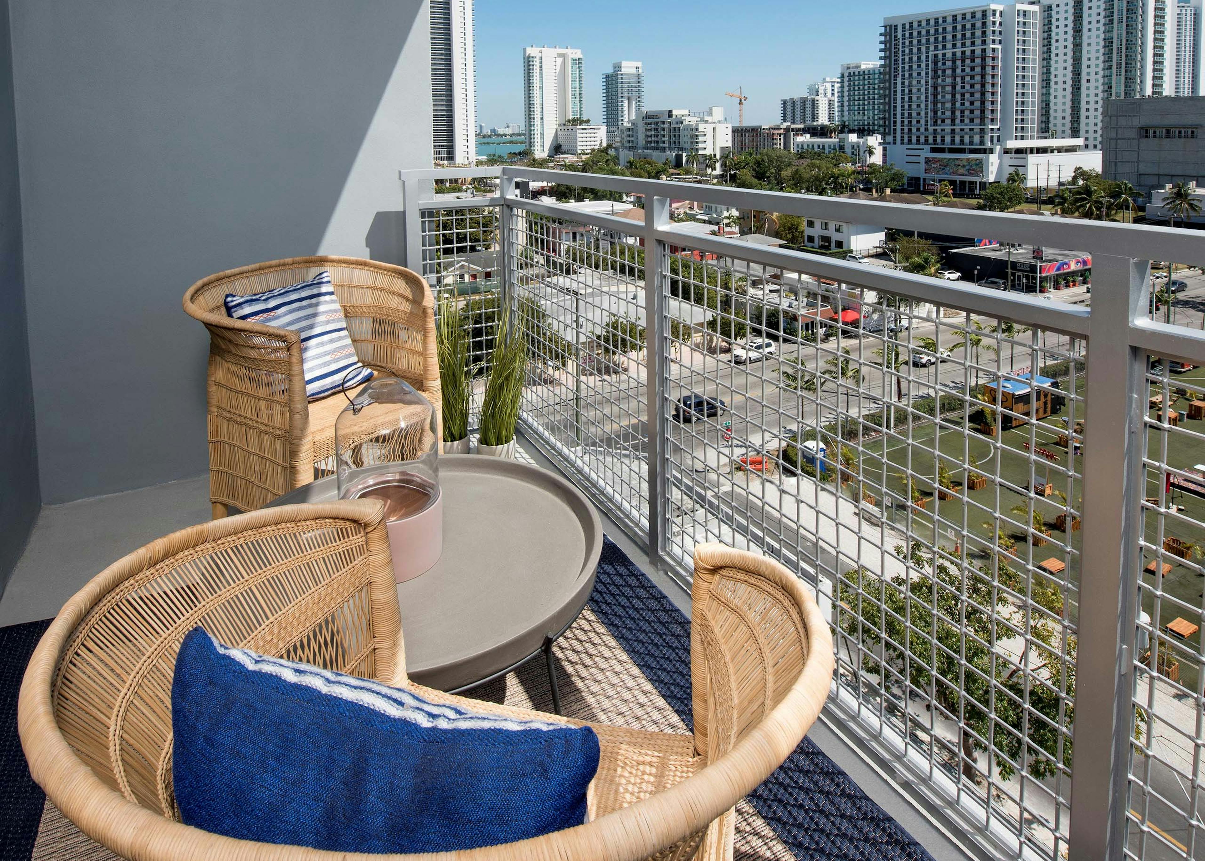 City view from balcony at AMLI Midtown 29 apartments with metal railing and wicker chairs with blue striped pillows and table