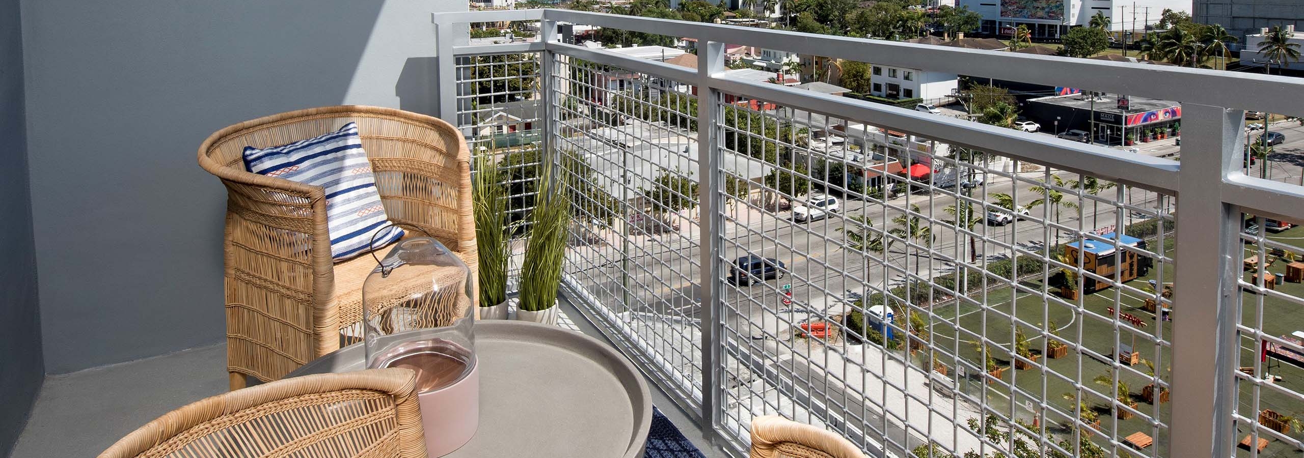 City view from balcony at AMLI Midtown 29 apartments with metal railing and wicker chairs with blue striped pillows and table