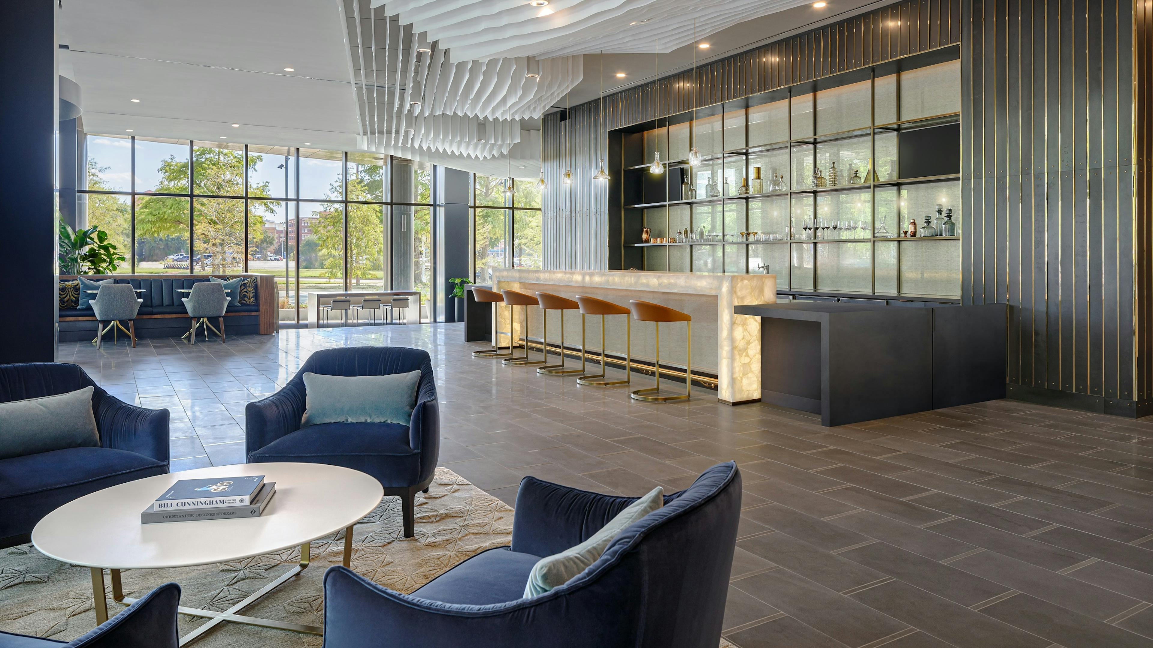 Resident lounge at AMLI Fountain Place with 4 blue velvet chairs and modern bar with 5 stools and wall of windows in rear