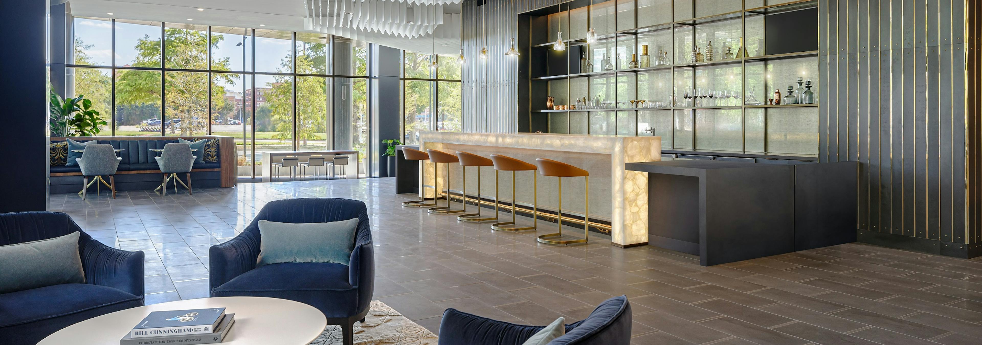 Resident lounge at AMLI Fountain Place with 4 blue velvet chairs and modern bar with 5 stools and wall of windows in rear