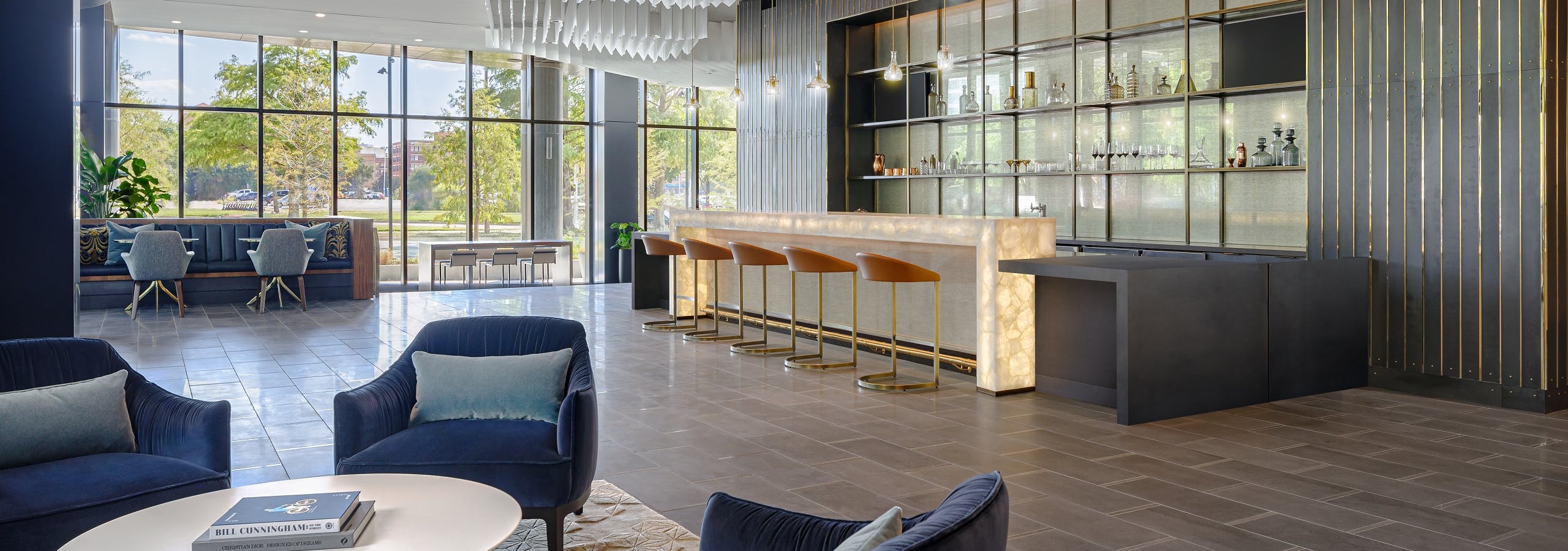 Resident lounge at AMLI Fountain Place with 4 blue velvet chairs and modern bar with 5 stools and wall of windows in rear