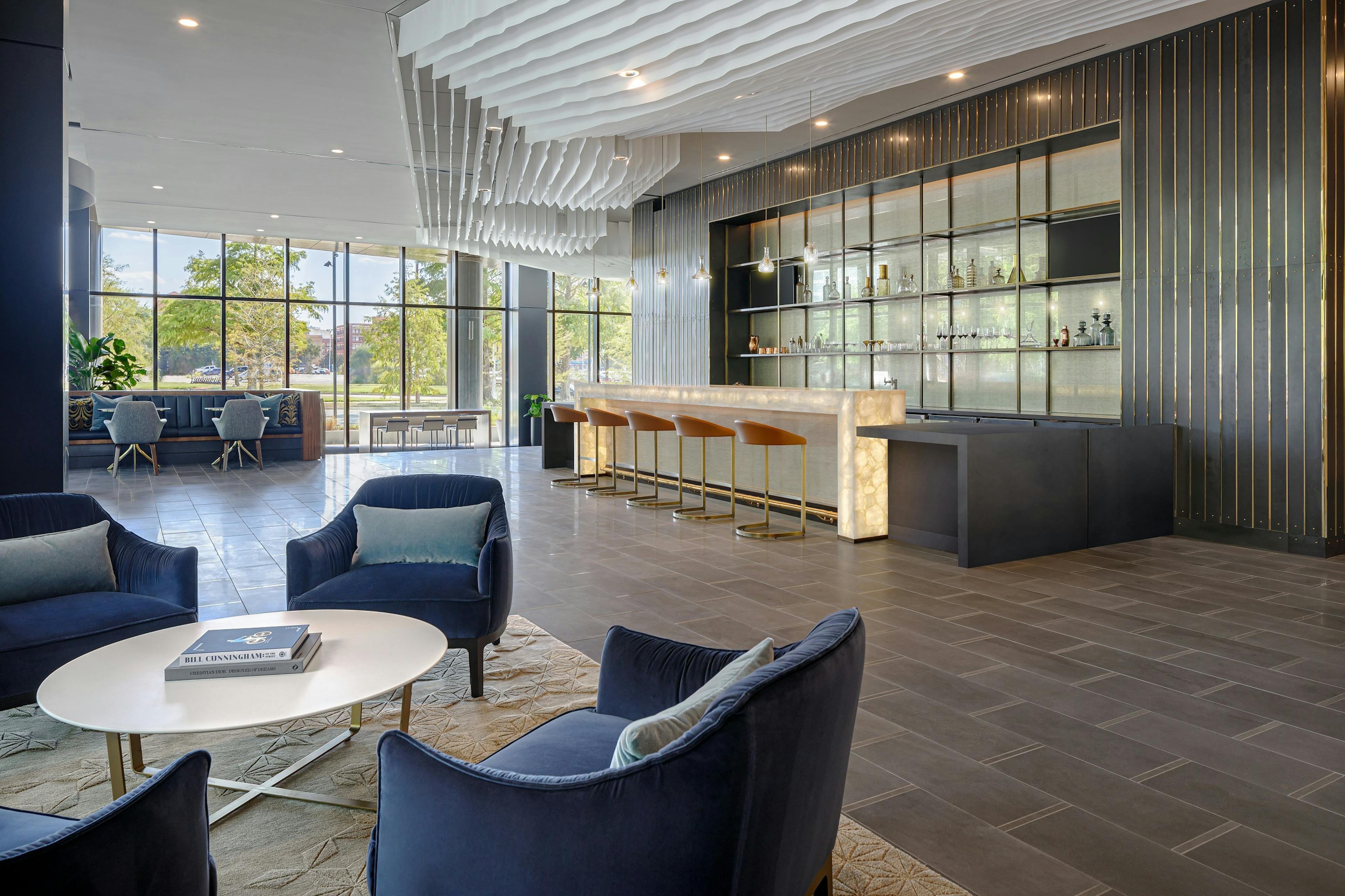 Resident lounge at AMLI Fountain Place with 4 blue velvet chairs and modern bar with 5 stools and wall of windows in rear