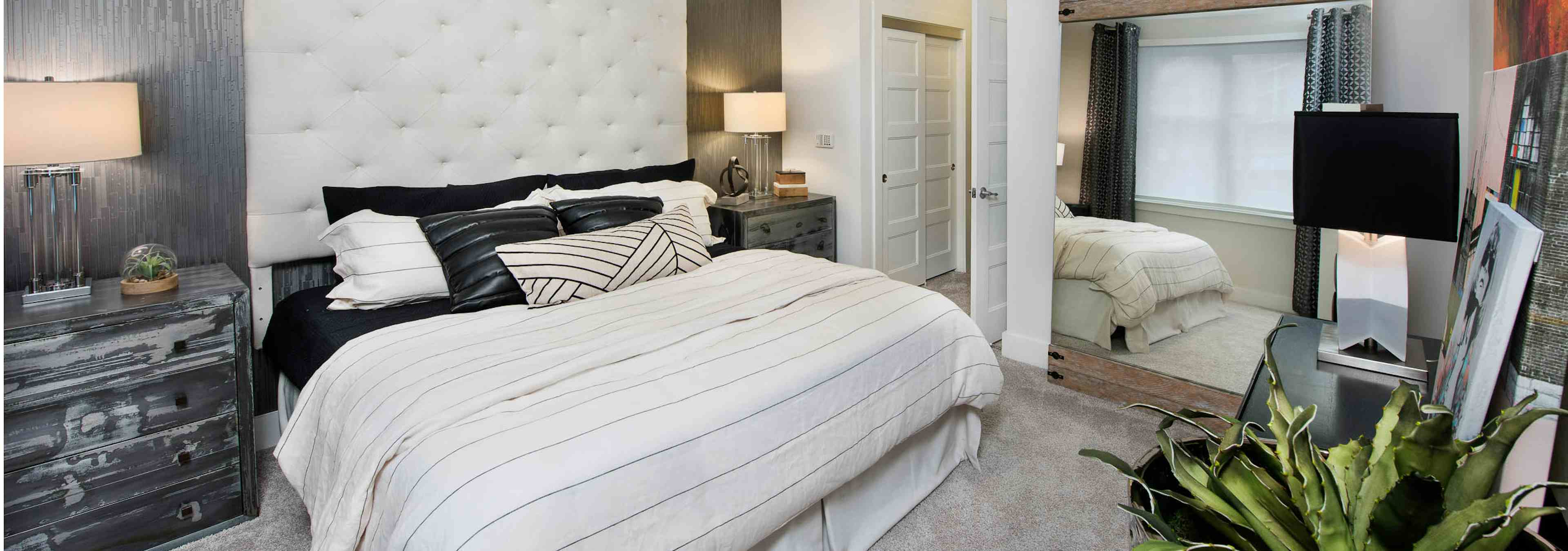 AMLI Buckhead bedroom with carpet and light walls with a tall ivory headboard and matching bedding with black throw pillows