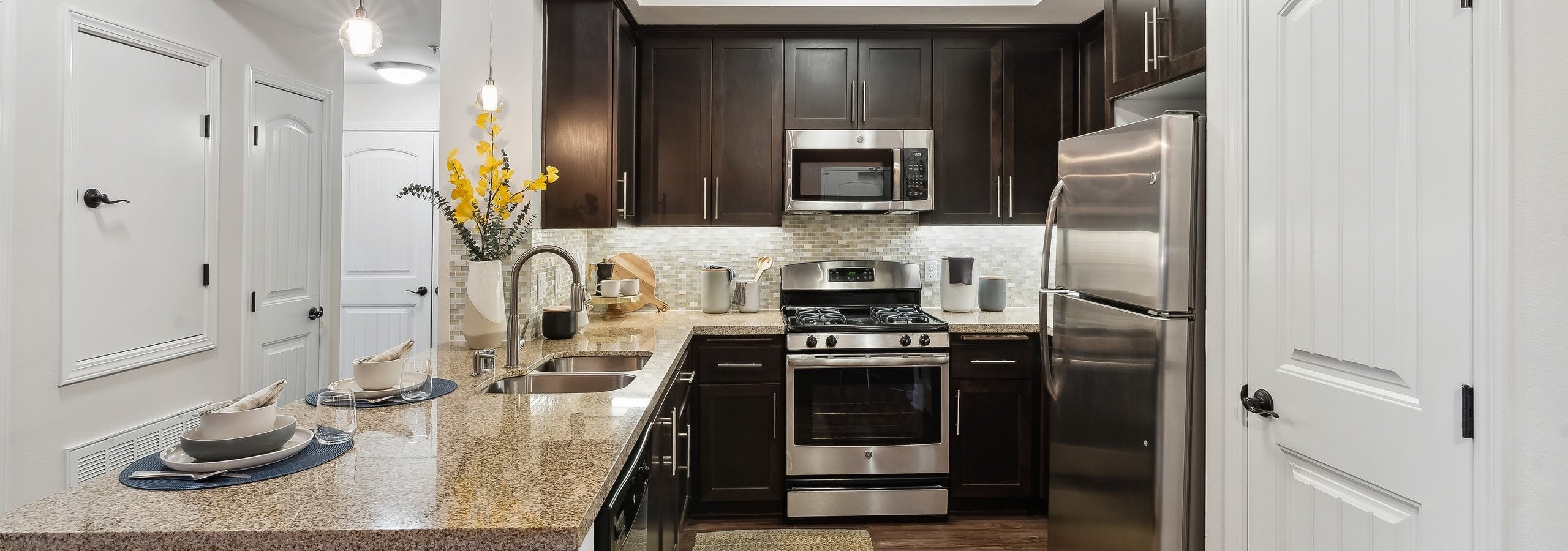 View of kitchen with dark wood cabinetry and gas range and granite countertops and hardwood flooring at AMLI Spanish Hills