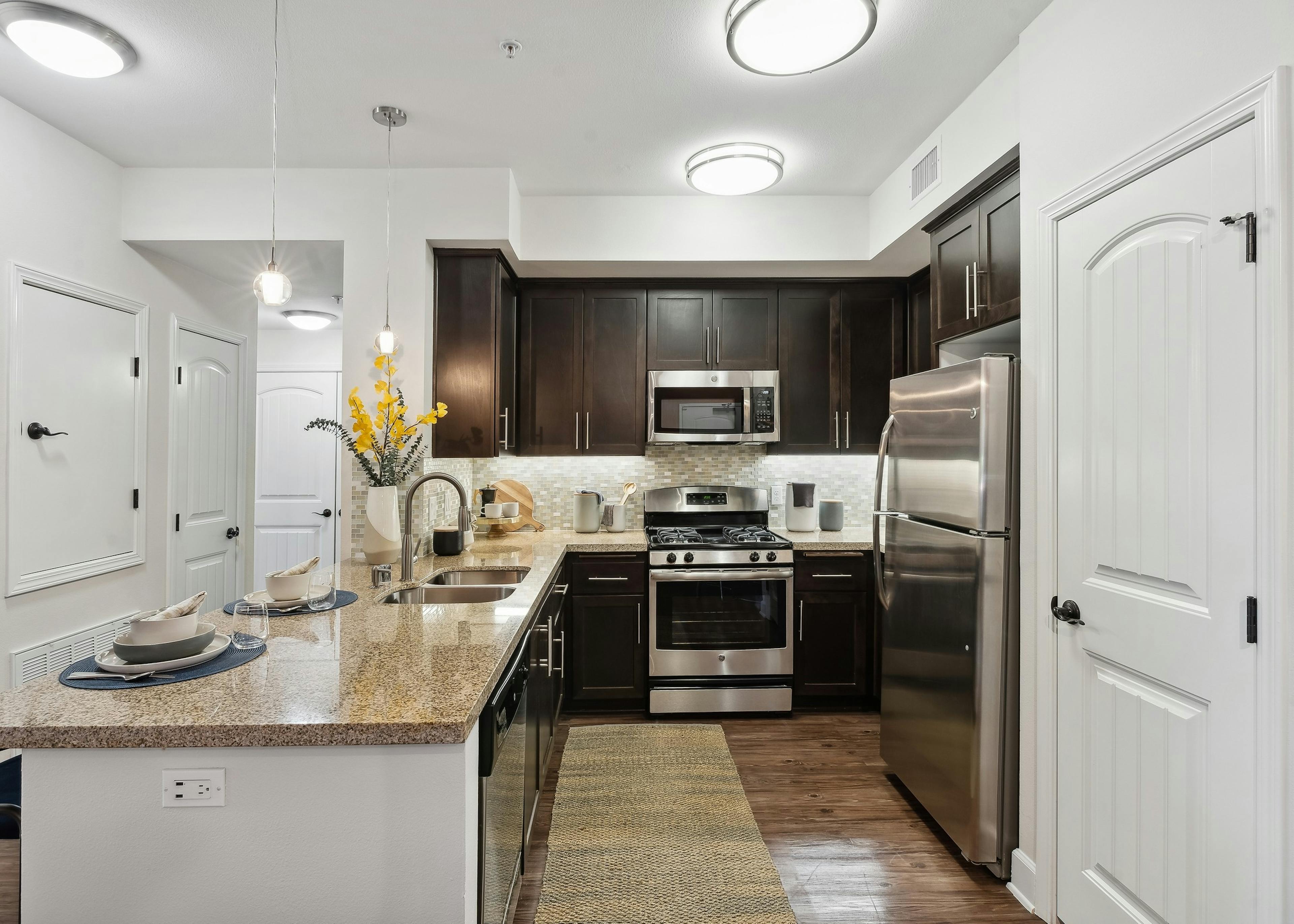View of kitchen with dark wood cabinetry and gas range and granite countertops and hardwood flooring at AMLI Spanish Hills