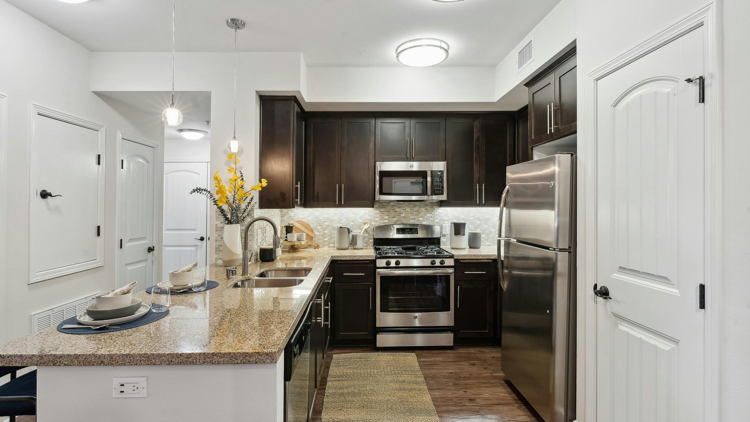 View of kitchen with dark wood cabinetry and gas range and granite countertops and hardwood flooring at AMLI Spanish Hills