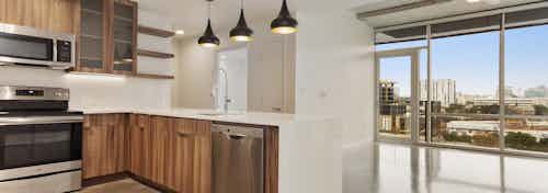 AMLI on 2nd kitchen with peek into living room with a bright city view through floor to ceiling windows along an entire wall