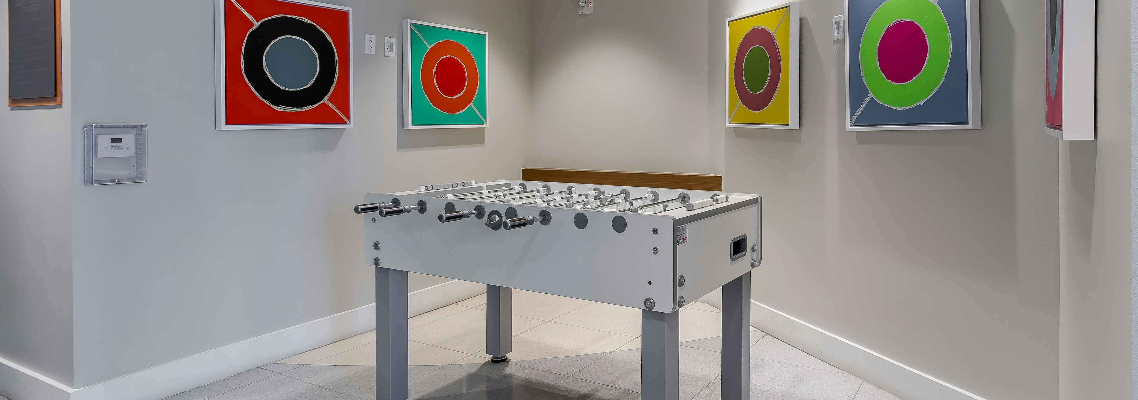 Interior view of the game room at AMLI 8800 apartments with a foosball table and colorful framed circle artwork on the wall