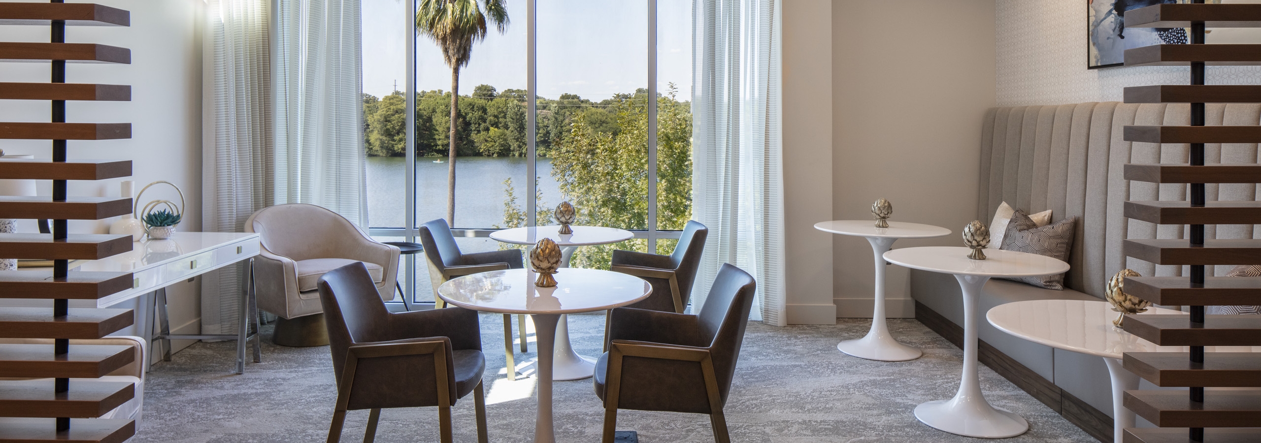 Coworking space at AMLI South Shore apartments with booth seating and brown chairs and white round tables with large windows