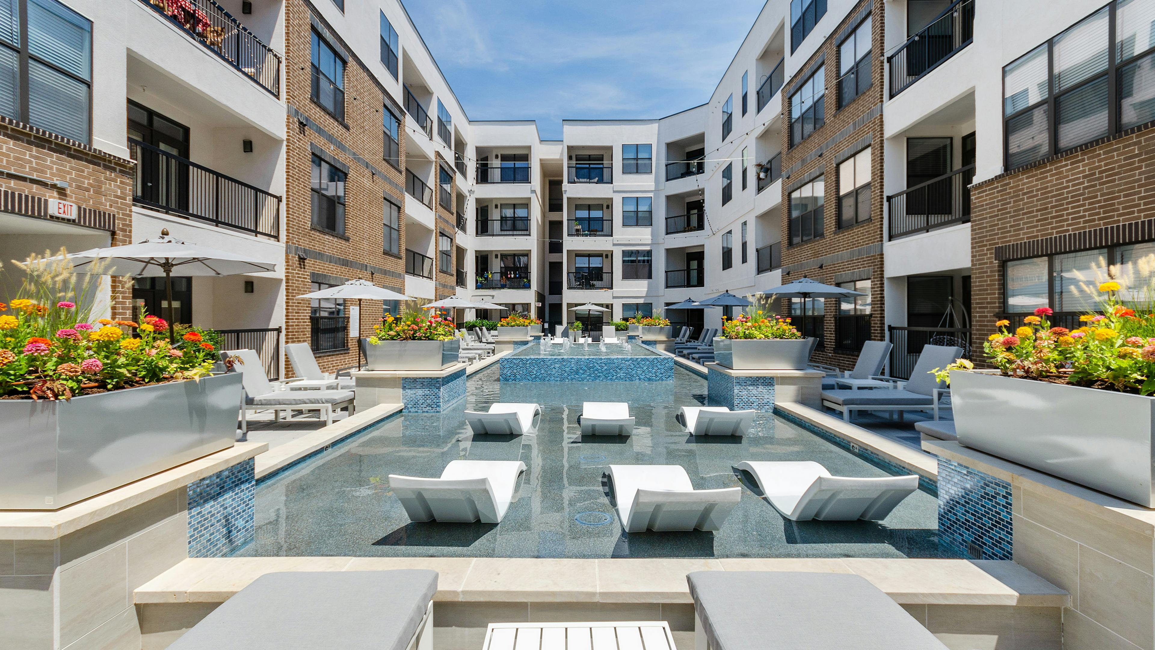 Daytime view of AMLI Quadrangle shallow pool with white in pool chaise loungers and a blue tile fountain in the center