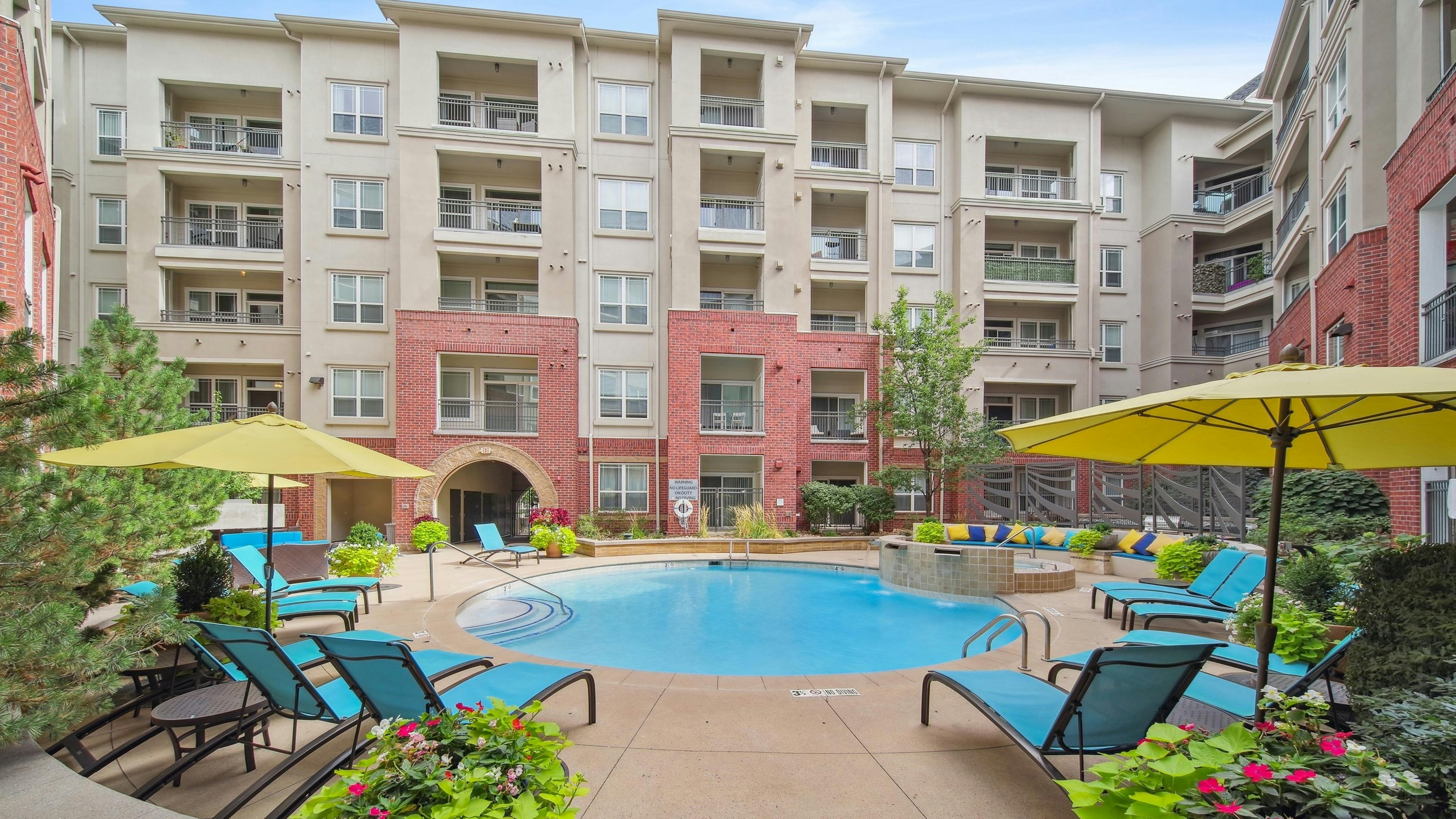 Daytime exterior view of the swimming pool at AMLI Park Avenue with blue sky and several lounge chairs and colorful plants