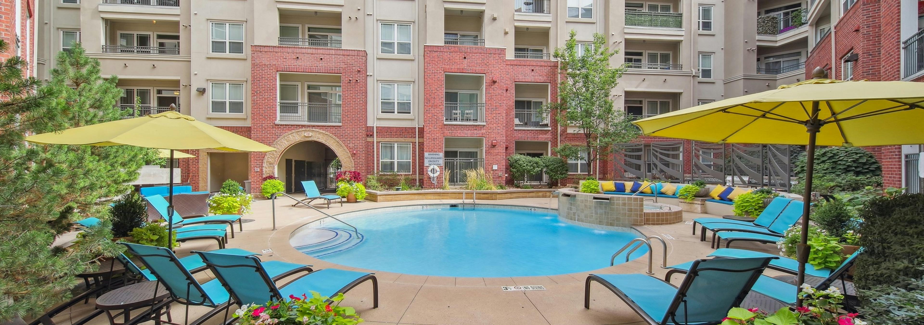 Daytime exterior view of the swimming pool at AMLI Park Avenue with blue sky and several lounge chairs and colorful plants