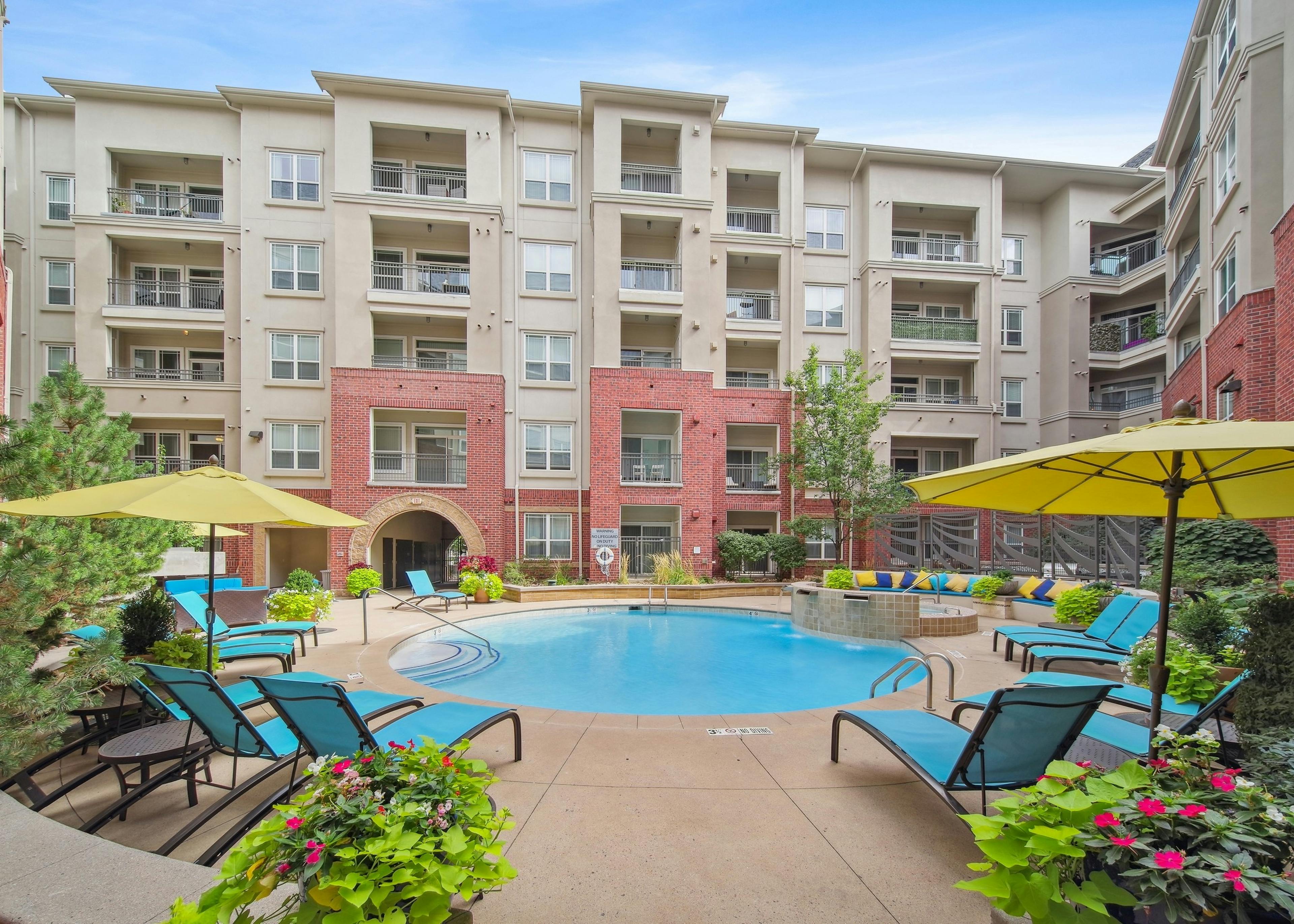 Daytime exterior view of the swimming pool at AMLI Park Avenue with blue sky and several lounge chairs and colorful plants