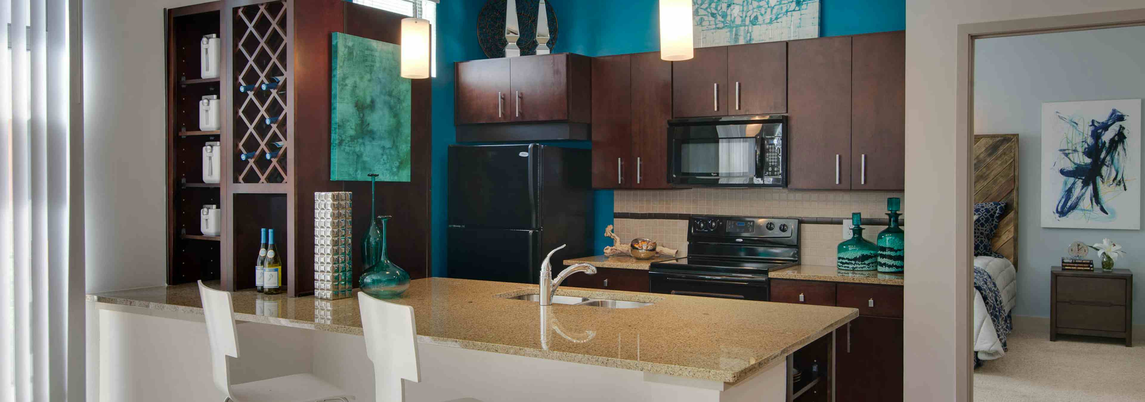 AMLI Old 4th Ward kitchen with light granite countertops and dark cabinetry with black appliances and a peek into the bedroom