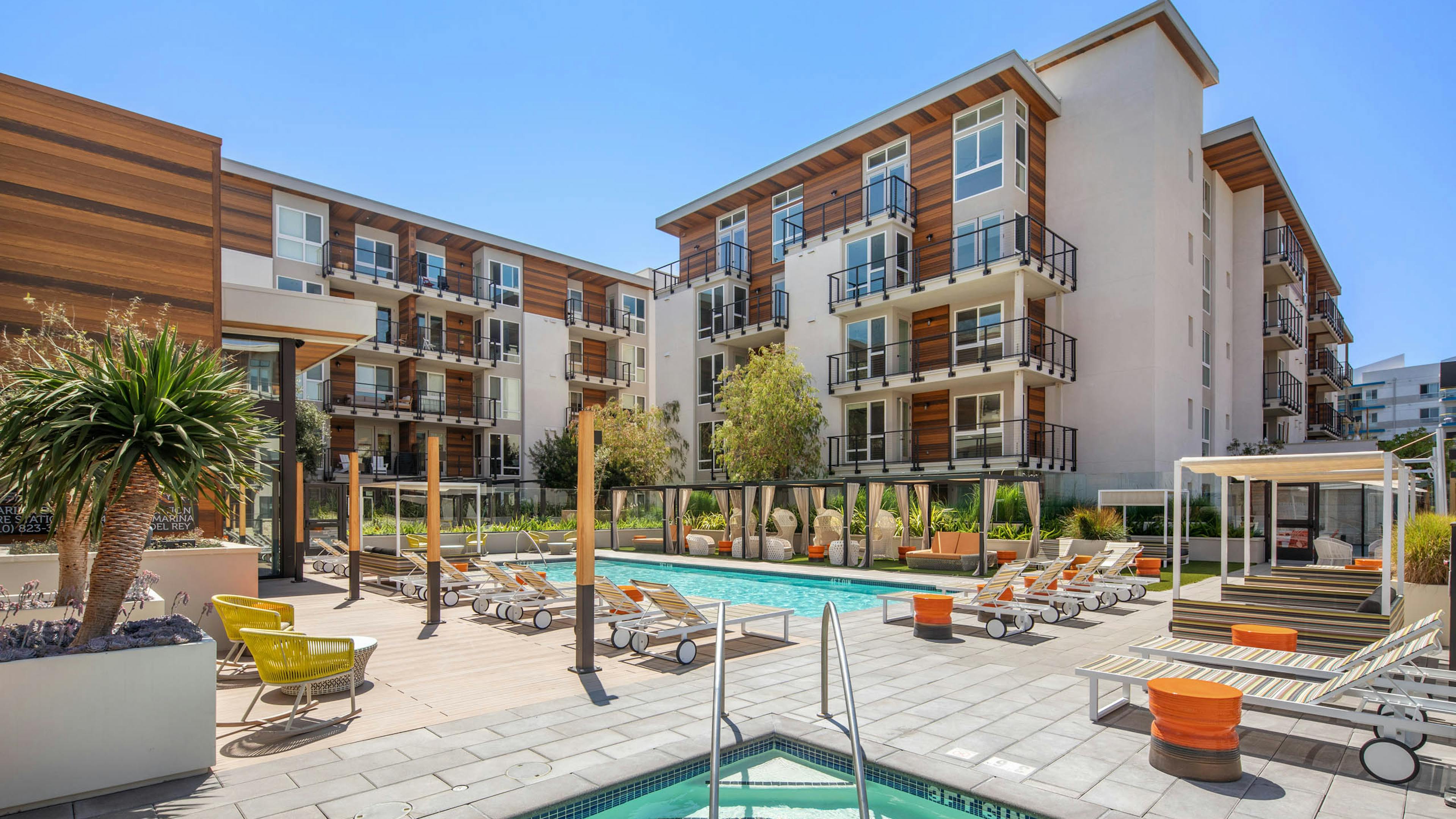 Sunny view of the AMLI Marina Del Rey swimming pool surrounded by apartments with various lounge seating and jacuzzi