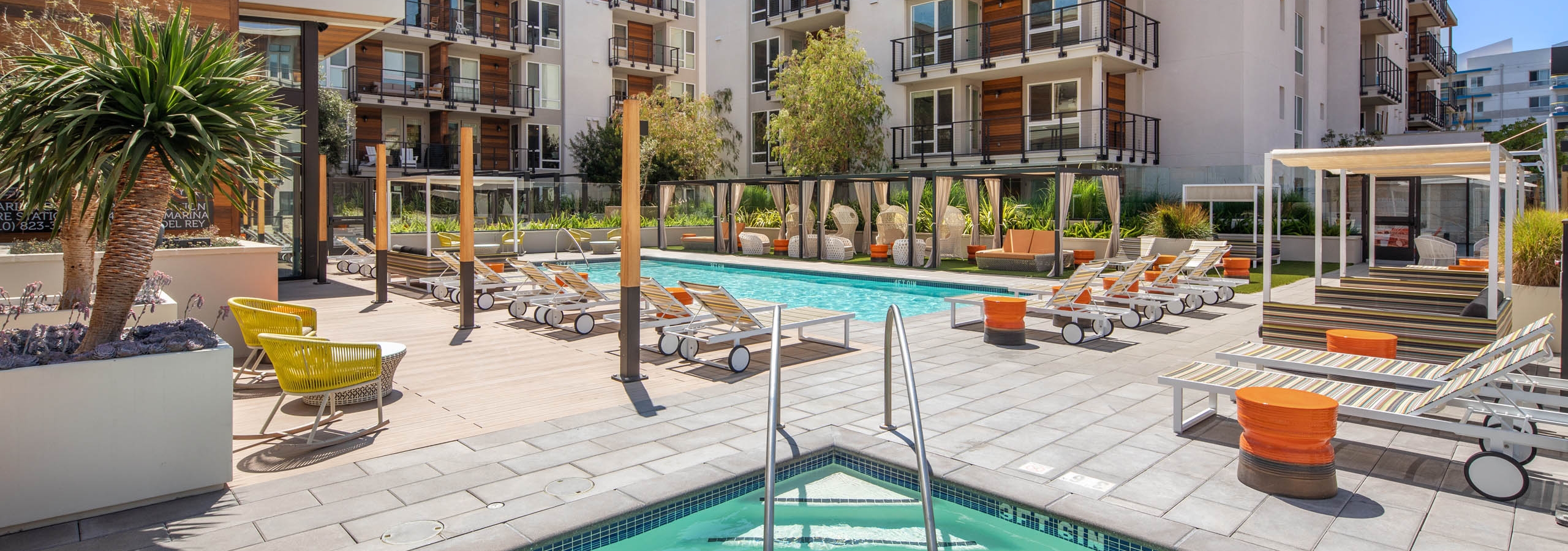 Sunny view of the AMLI Marina Del Rey swimming pool surrounded by apartments with various lounge seating and jacuzzi