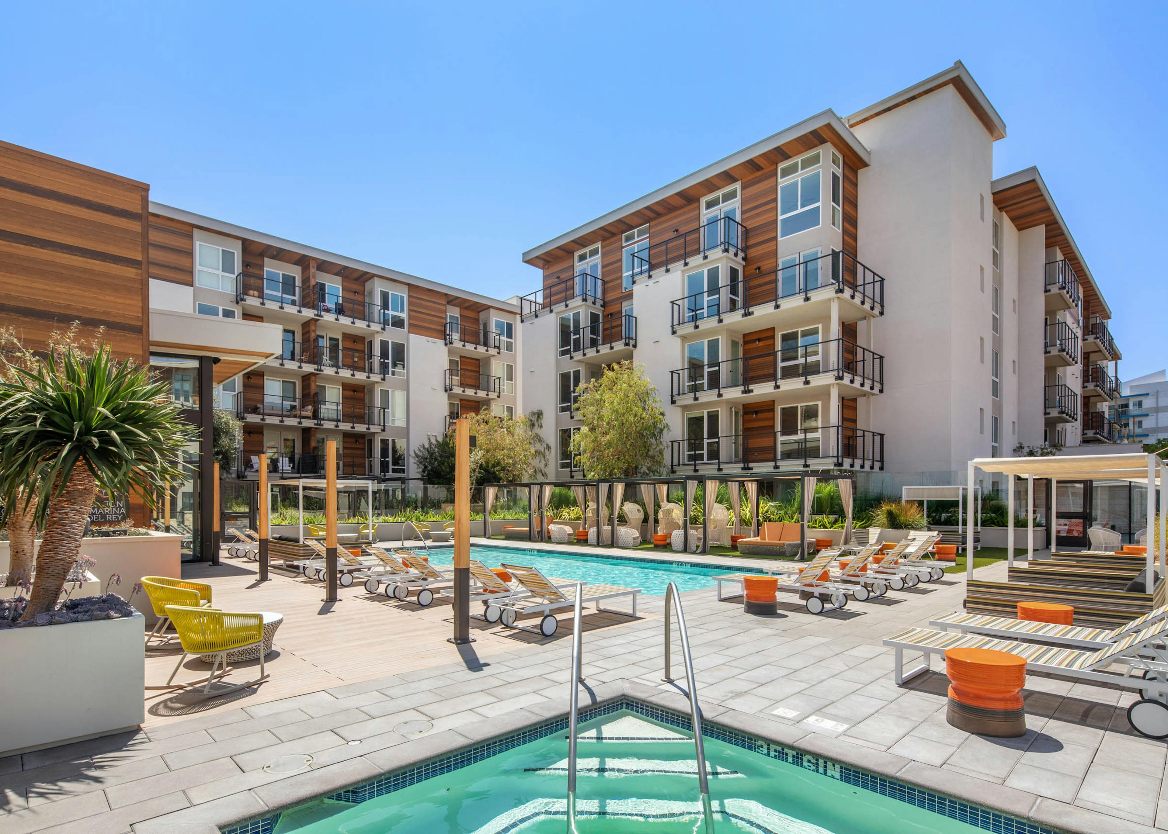 Sunny view of the AMLI Marina Del Rey swimming pool surrounded by apartments with various lounge seating and jacuzzi
