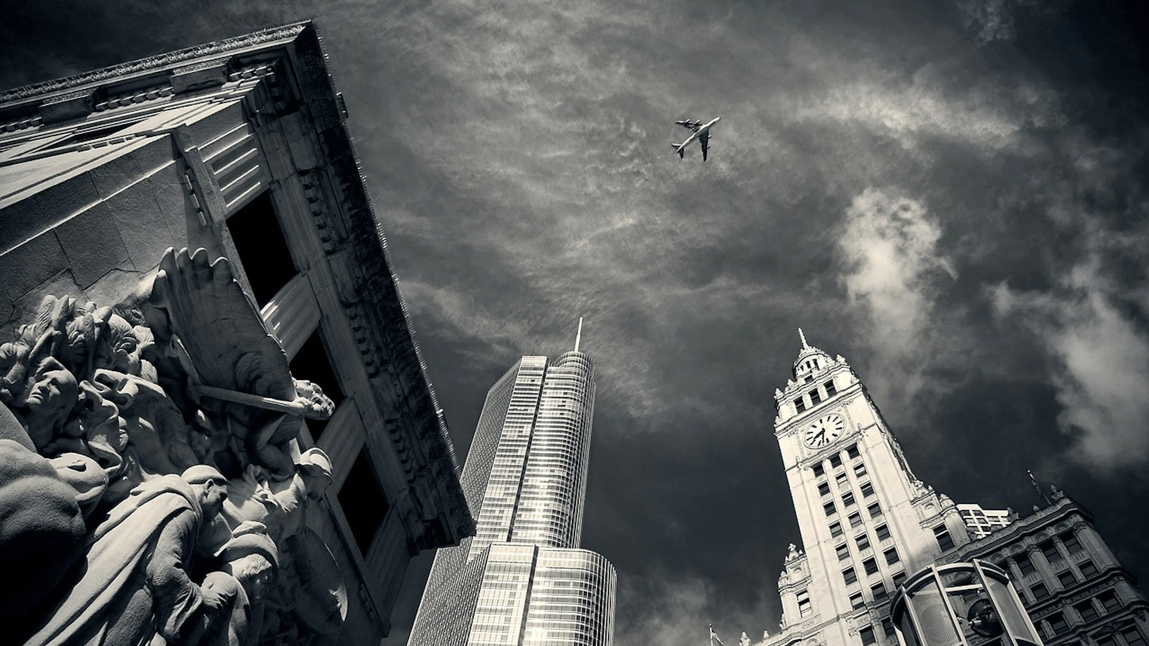 Black and white image of a statue and three skyscrapers taken from the ground looking up at the sky from the streets in Chicago