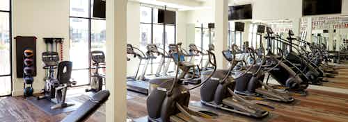 AMLI on Riverside fitness center with exercise machines facing floor to ceiling windows and large TVs hanging on the walls