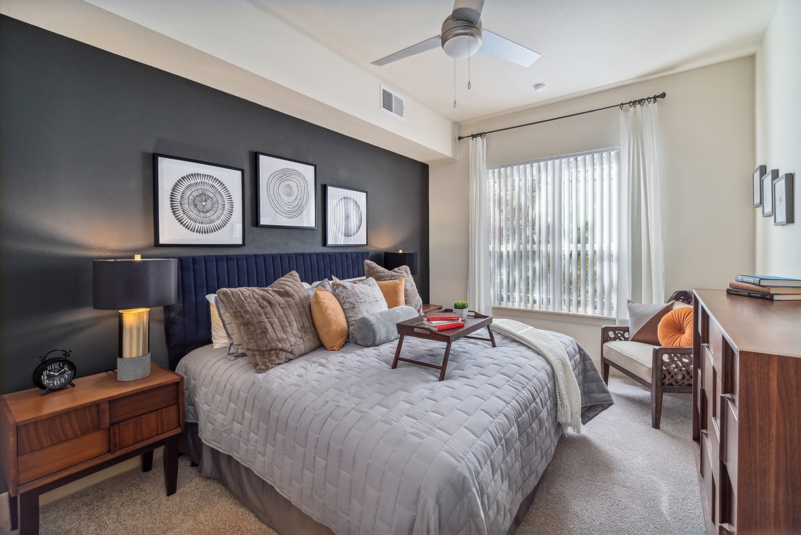 Bedroom at AMLI Park Avenue with a large bed and nightstand across from dresser and a window with blinds