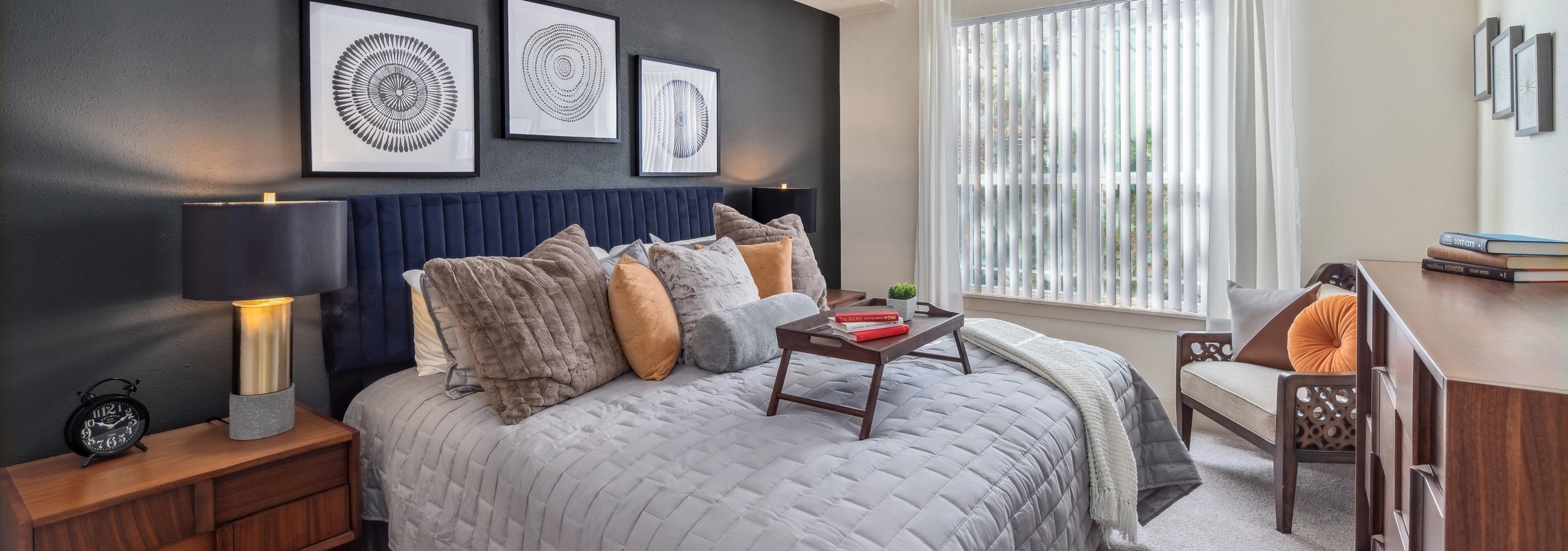 Bedroom at AMLI Park Avenue with a large bed and nightstand across from dresser and a window with blinds
