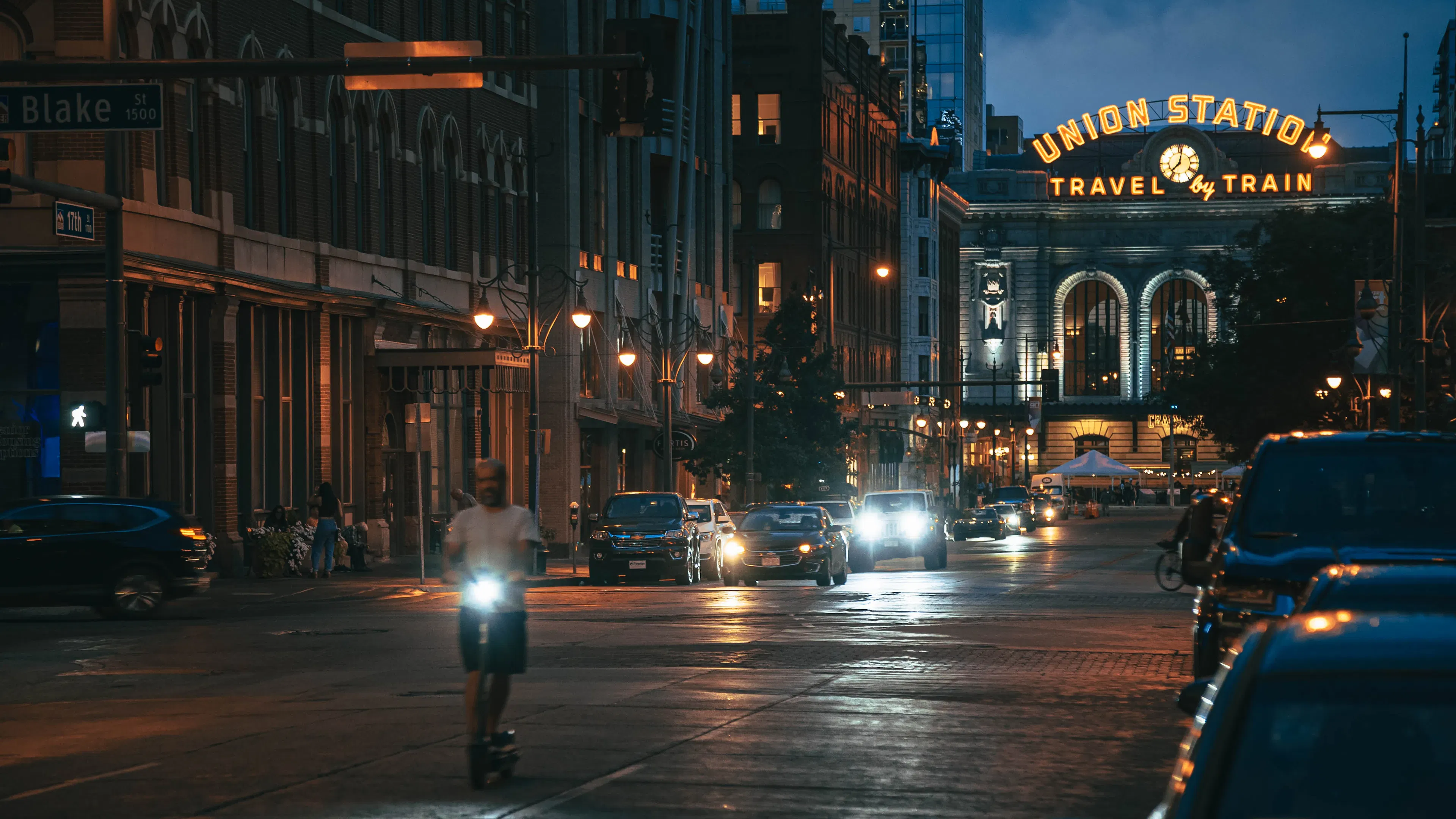 A man on a scooter rides away from Denver's Union Station with traffic behind him at night