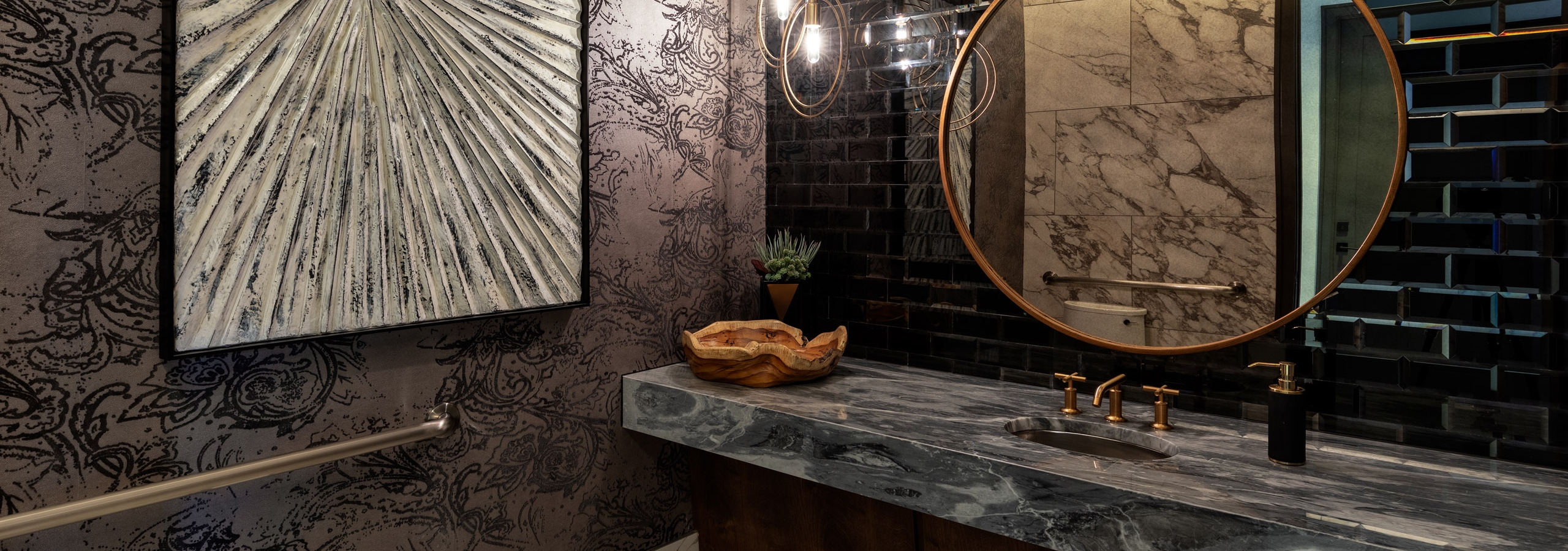 Interior view of AMLI Grapevine clubhouse bathroom with brass finishes and a glass brick backsplash and large circular mirror