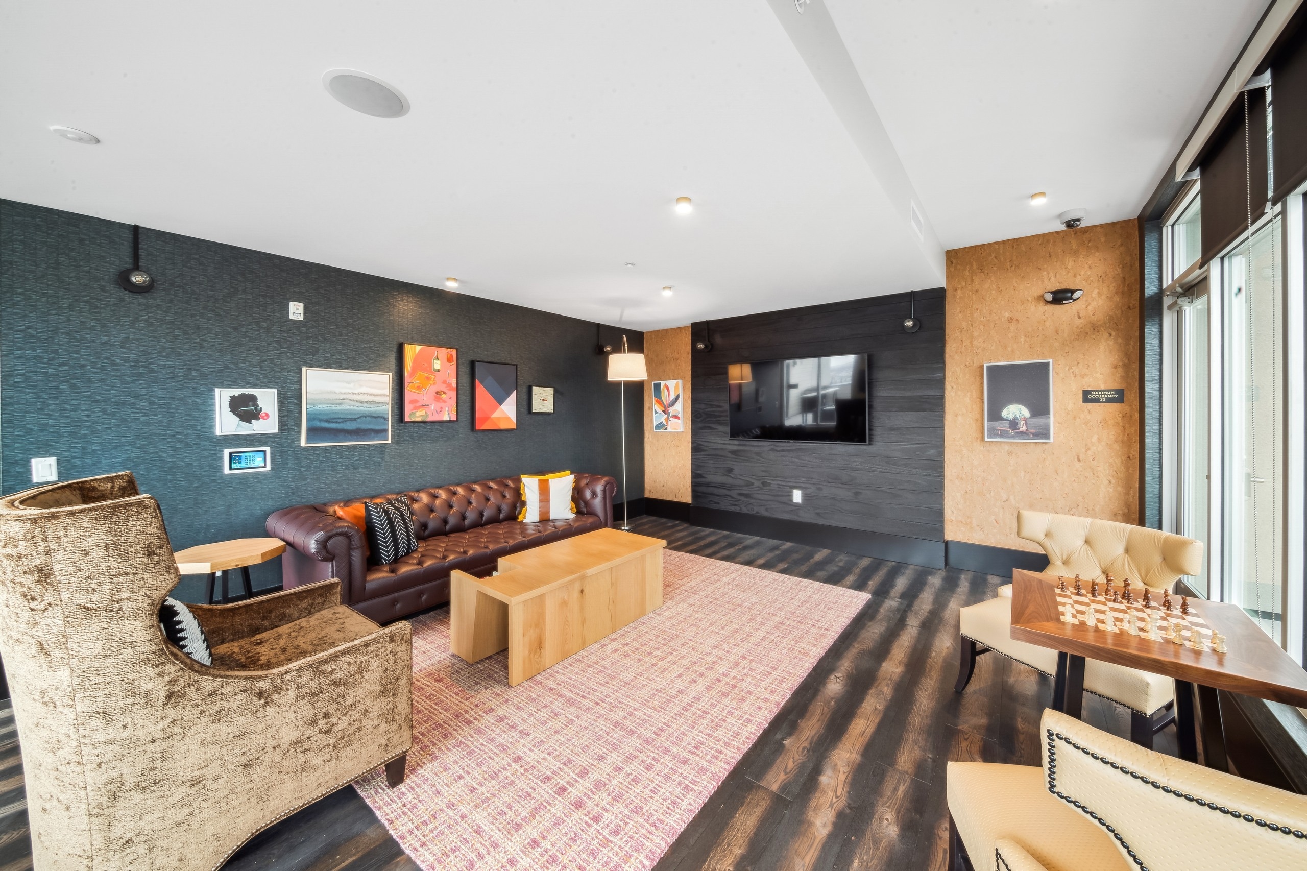 AMLI RiNo skydeck lounge with brown leather tufted couch and other seating on dark walls with artwork and a flat screen TV 