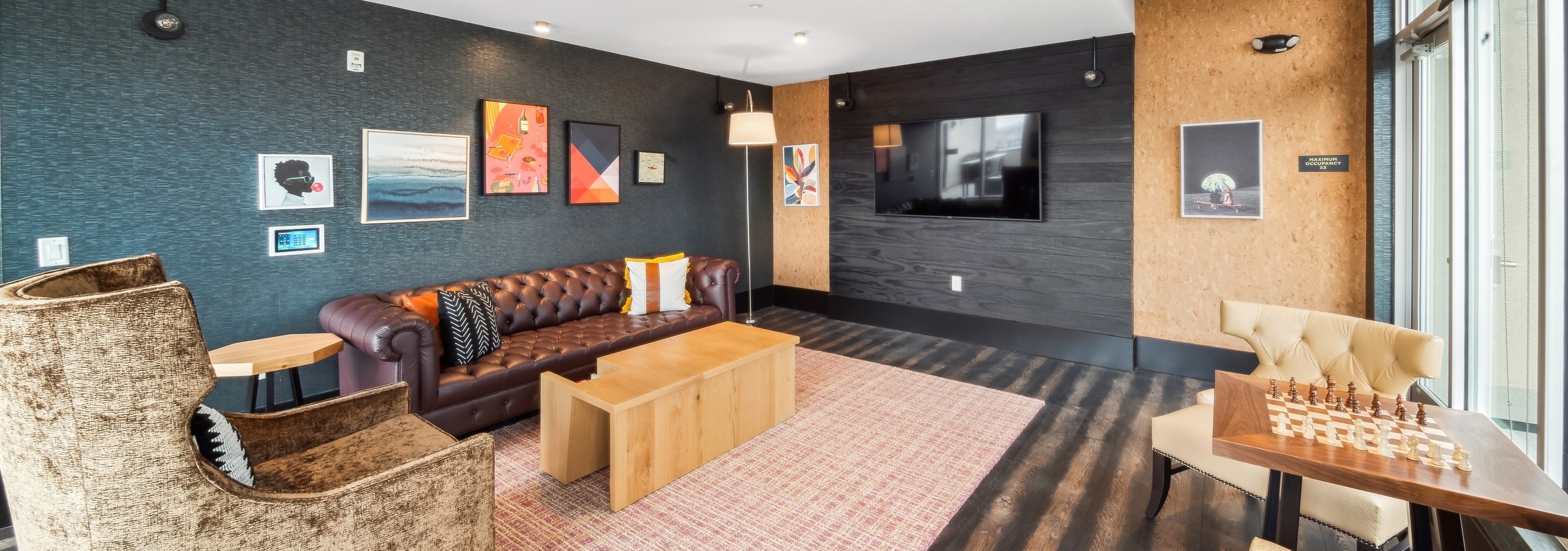 AMLI RiNo skydeck lounge with brown leather tufted couch and other seating on dark walls with artwork and a flat screen TV