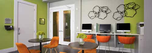 Interior of business center at AMLI 5350 with lime green and grey walls with three desktop computers and orange office chairs