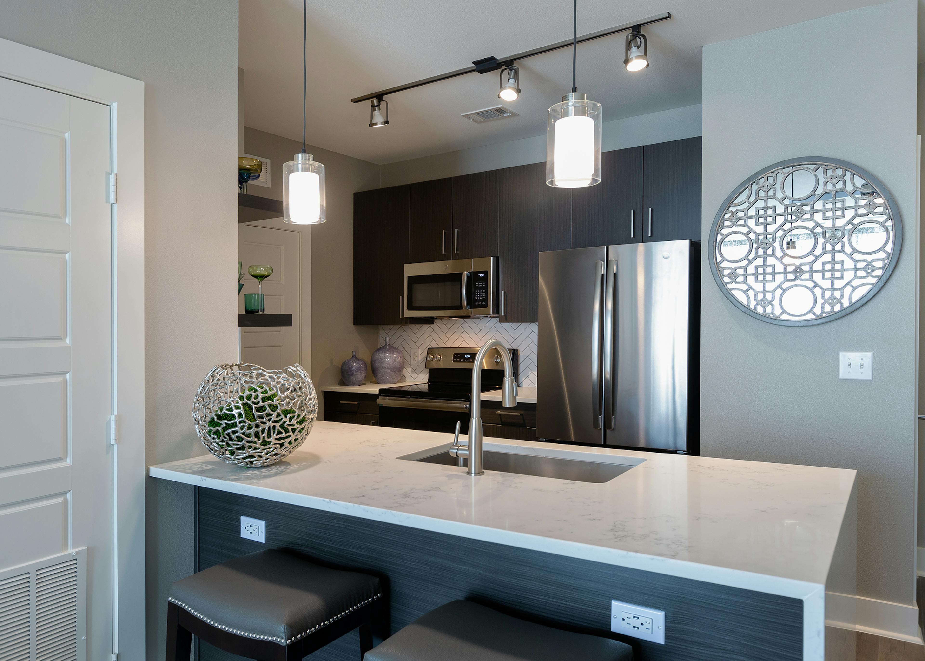 AMLI South Shore white counter with quartz countertop and barstools with view of stainless steel appliances in background