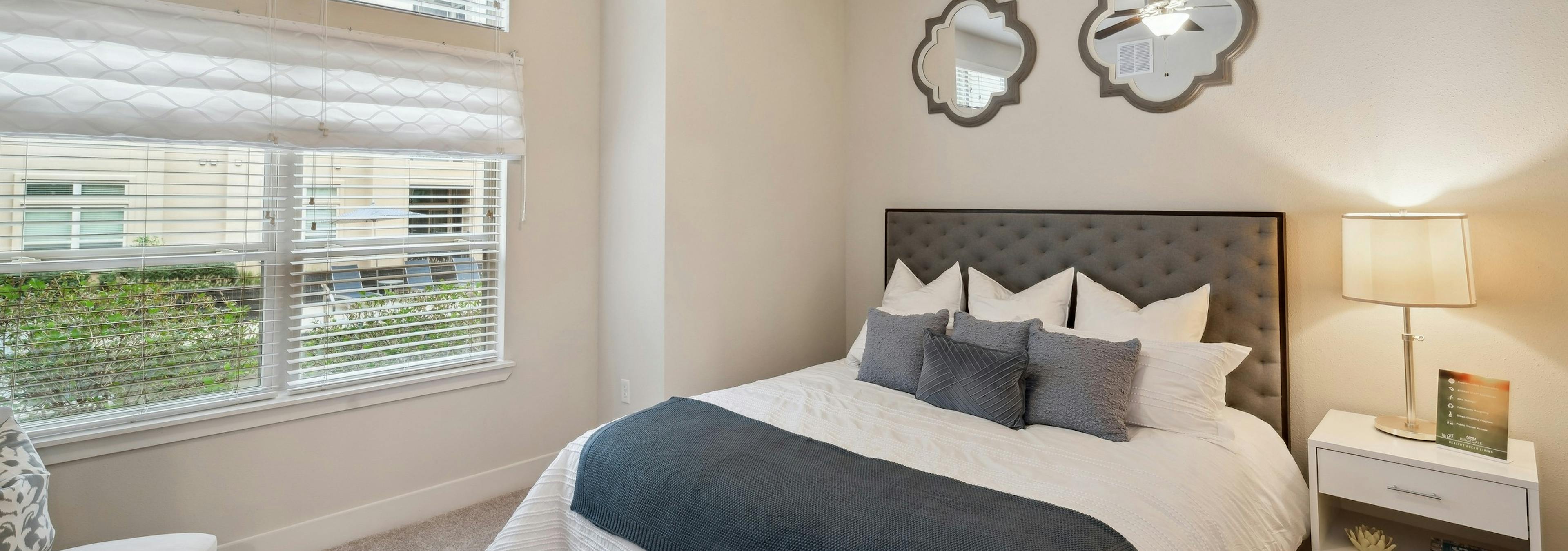 Interior view of a bedroom at AMLI RidgeGate with a king size bed with side table and an overhead fan and 2 decorative mirrors
