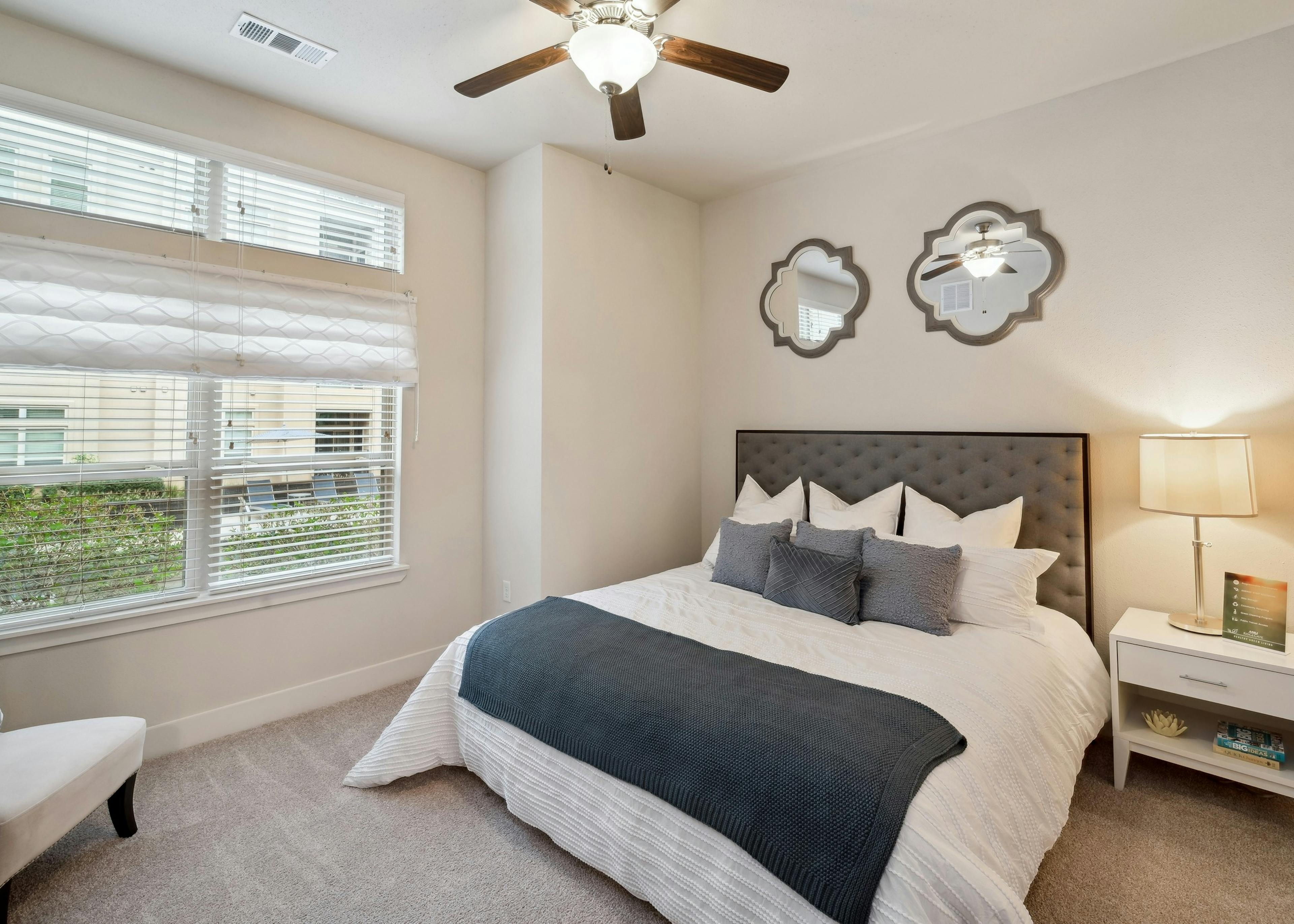 Interior view of a bedroom at AMLI RidgeGate with a king size bed with side table and an overhead fan and 2 decorative mirrors
