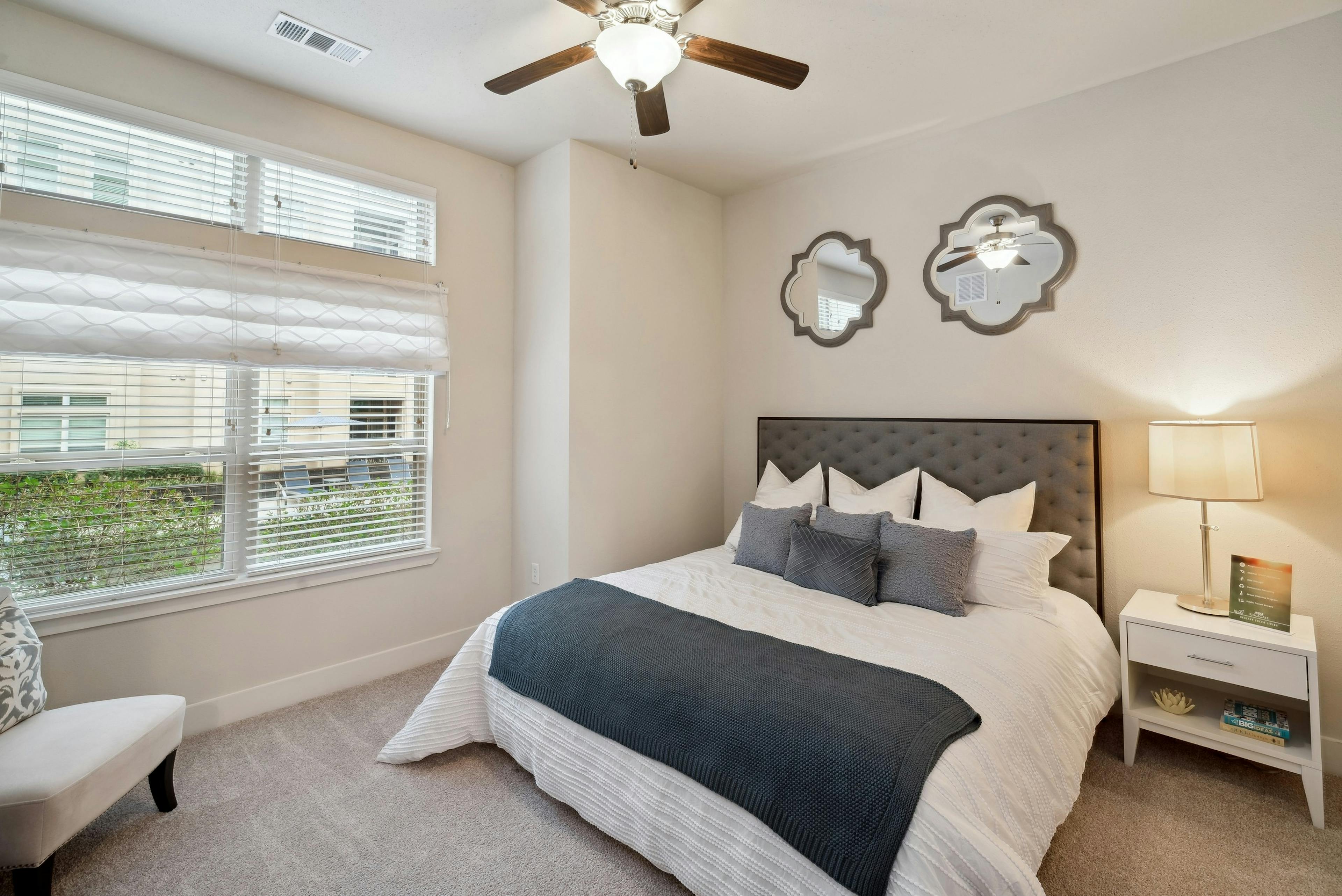 Interior view of a bedroom at AMLI RidgeGate with a king size bed with side table and an overhead fan and 2 decorative mirrors