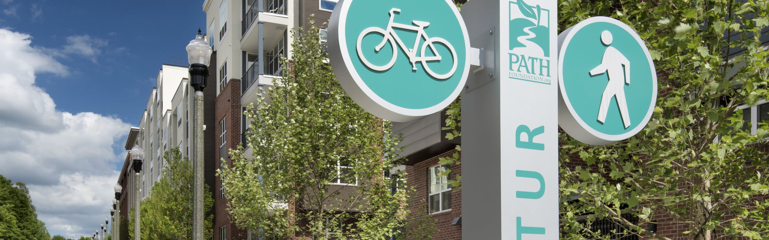 Exterior daytime view of AMLI Decatur apartments with the PATH Fountain’s bike path and sidewalk in front of the building