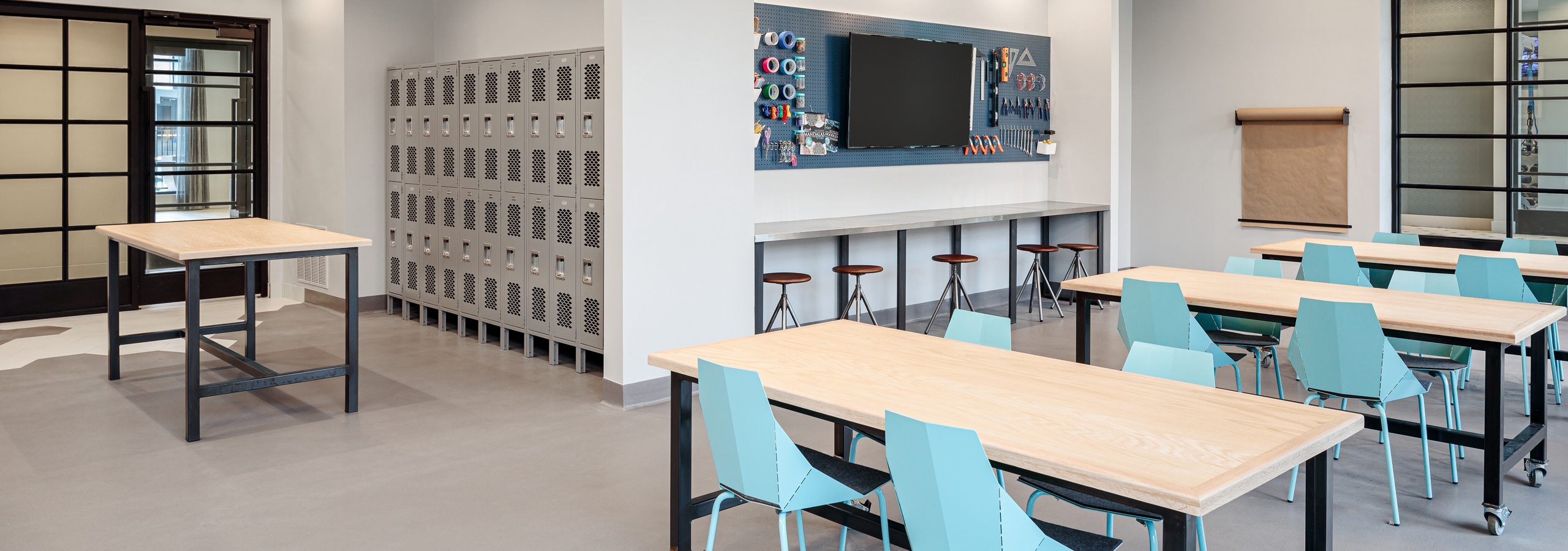Close up of wooden tables with light blue chairs in the maker space at AMLI Addison with a large work table in the background