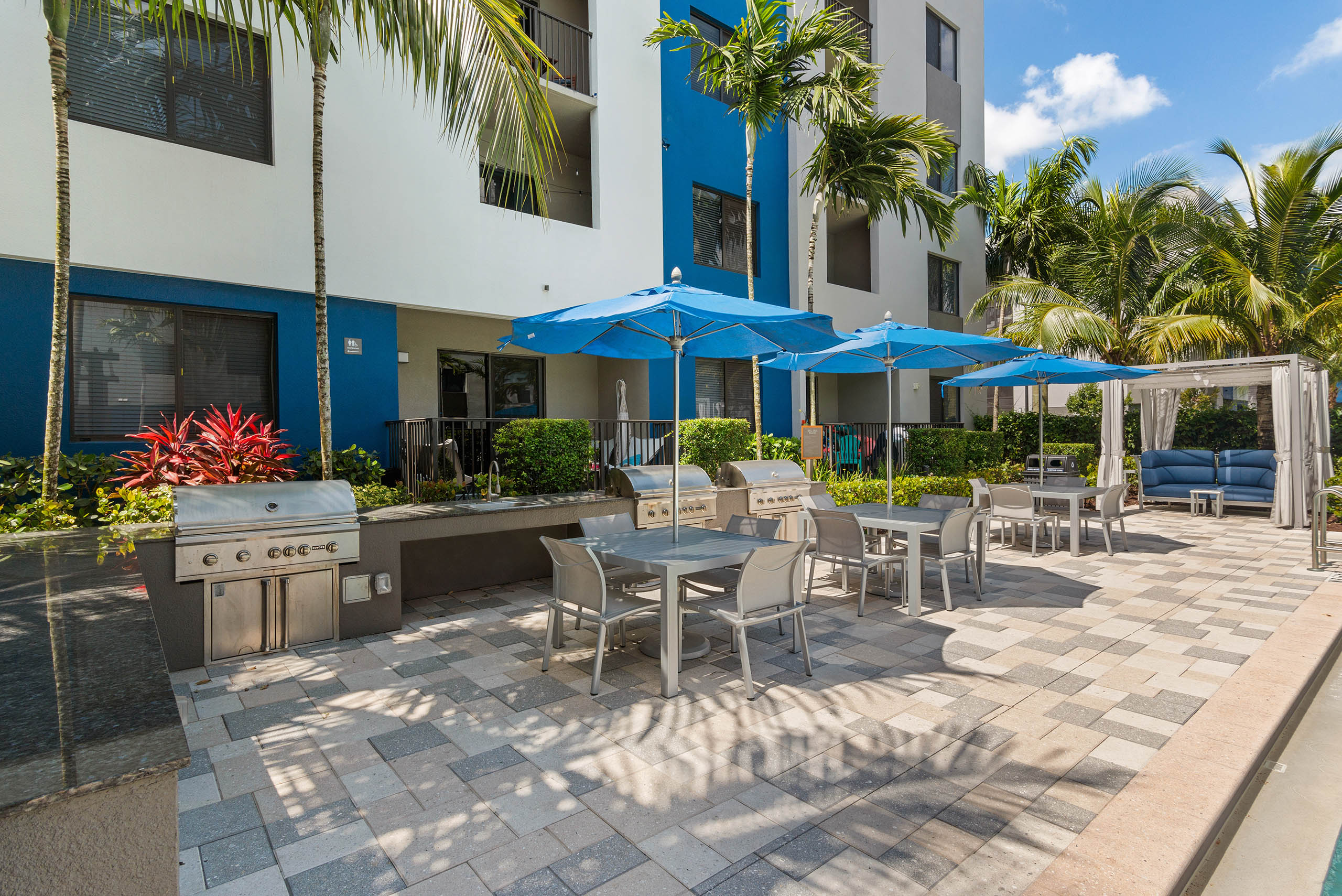 The grill station at AMLI 8800 with steel grills and granite counters and table and chairs with blue umbrellas and a cabana