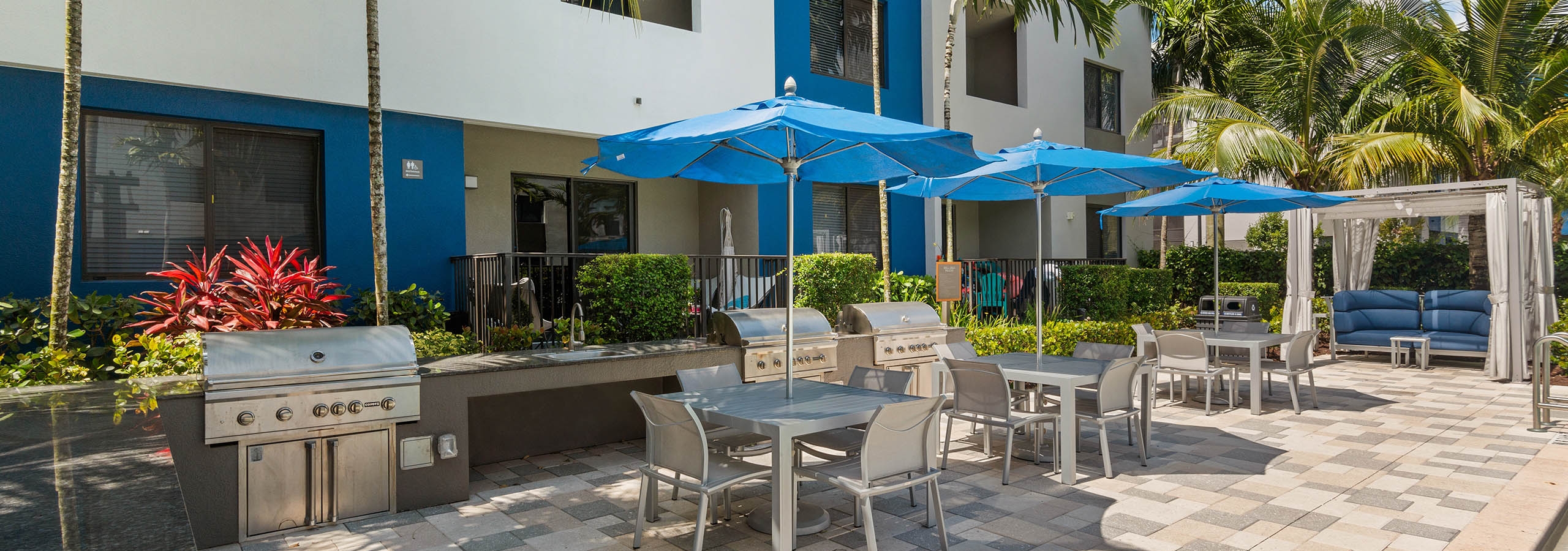 The grill station at AMLI 8800 with steel grills and granite counters and table and chairs with blue umbrellas and a cabana