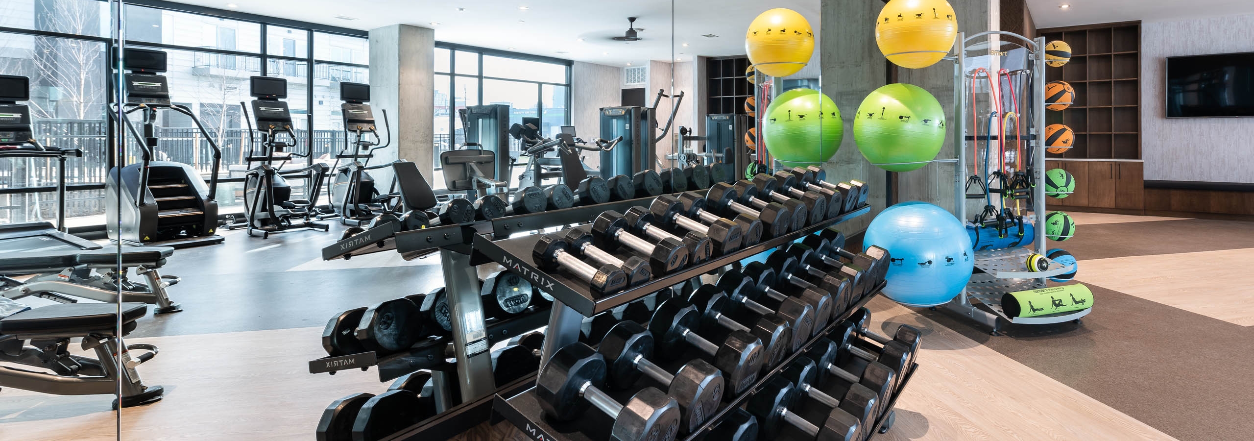 Fitness center at AMLI Art District with weights and yoga mats and medicine balls and a large mirror showing cardio equipment