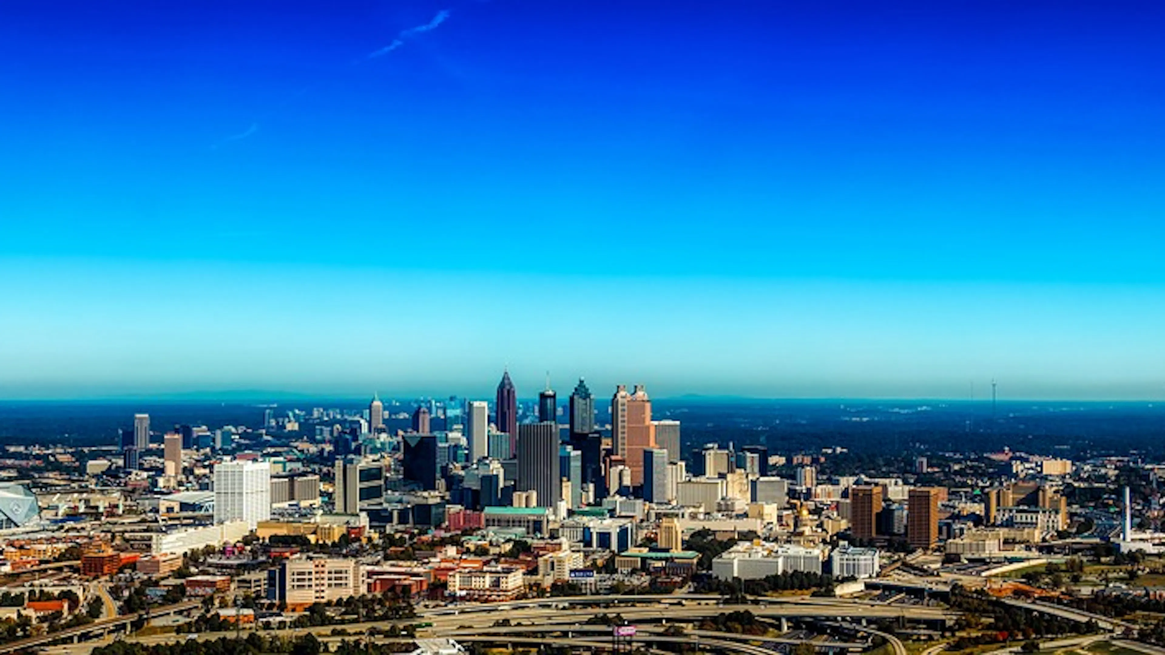 Wide shot of Atlanta's skyline with the highway and downtown skyscrapers under a clear blue sky