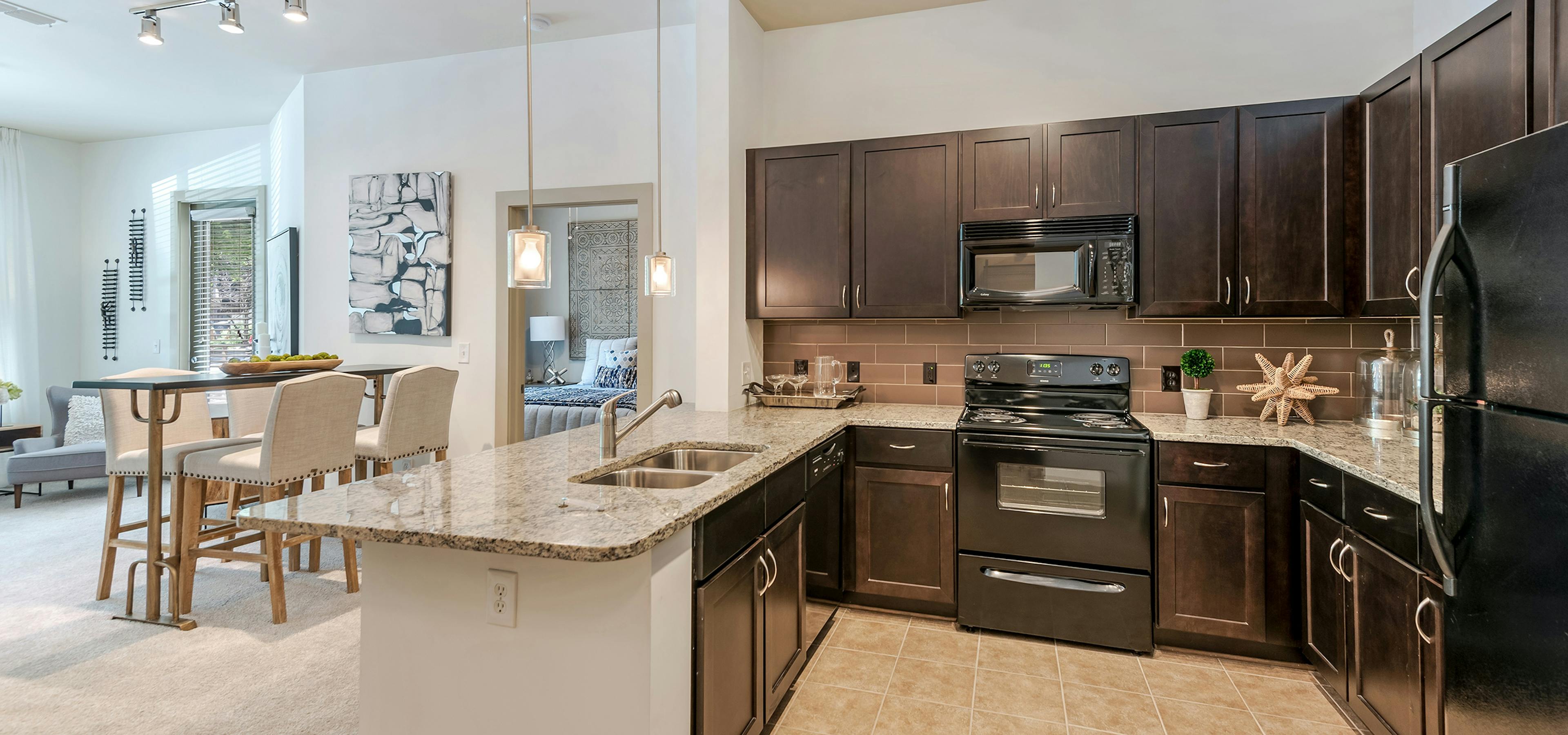AMLI Parkside apartment spacious kitchen with light tile and dark cabinetry and black appliances with peek into living room