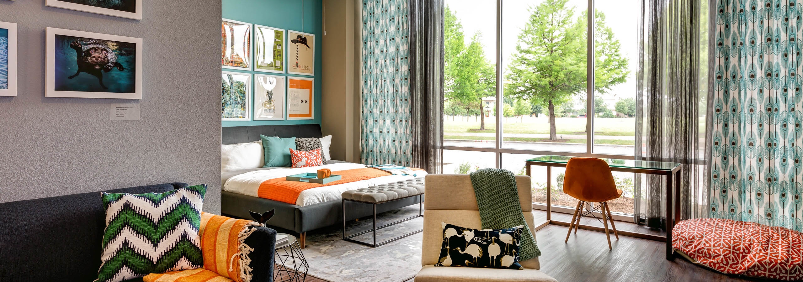 Bedroom at AMLI at Mueller with large floor to ceiling windows and dark wood floors with orange and blue decor accents