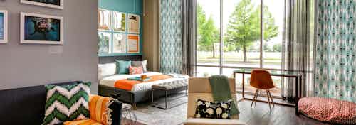 Bedroom at AMLI at Mueller with large floor to ceiling windows and dark wood floors with orange and blue decor accents