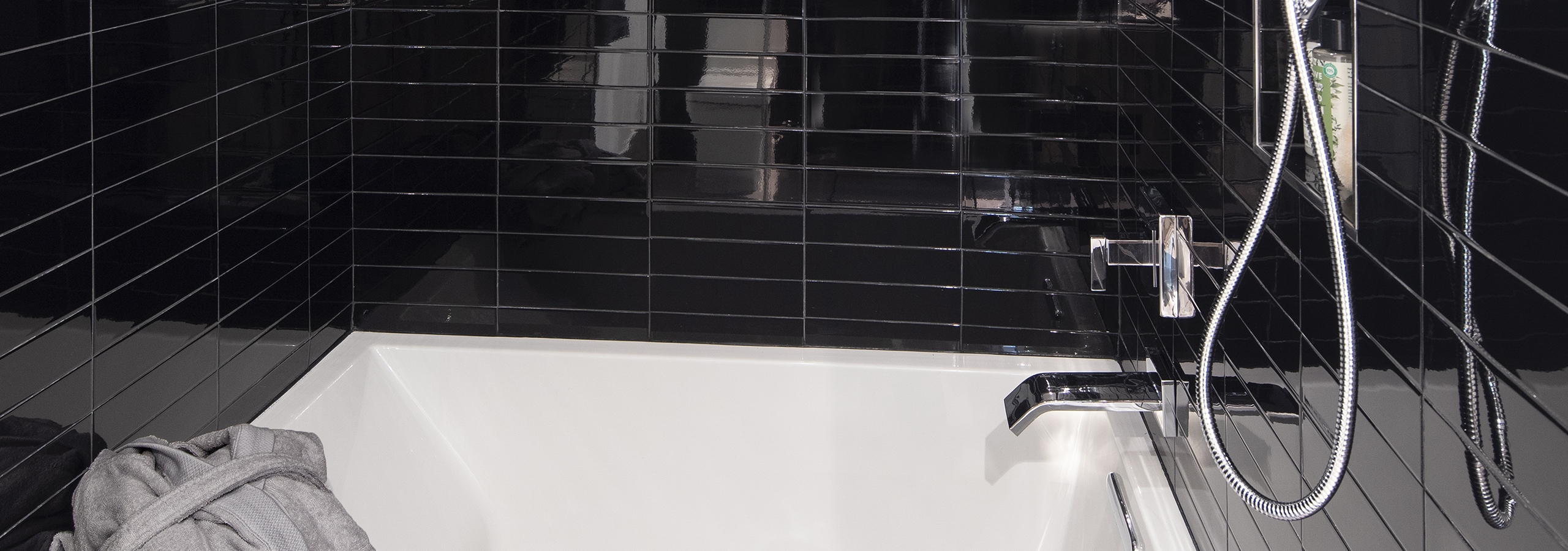 Interior of AMLI Midtown Miami apartment bathroom with black subway tile wall and soaking tub with rain shower