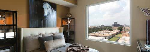 Interior view of AMLI Design District apartment bedroom with bed and painting of horse above it and window overlooking city