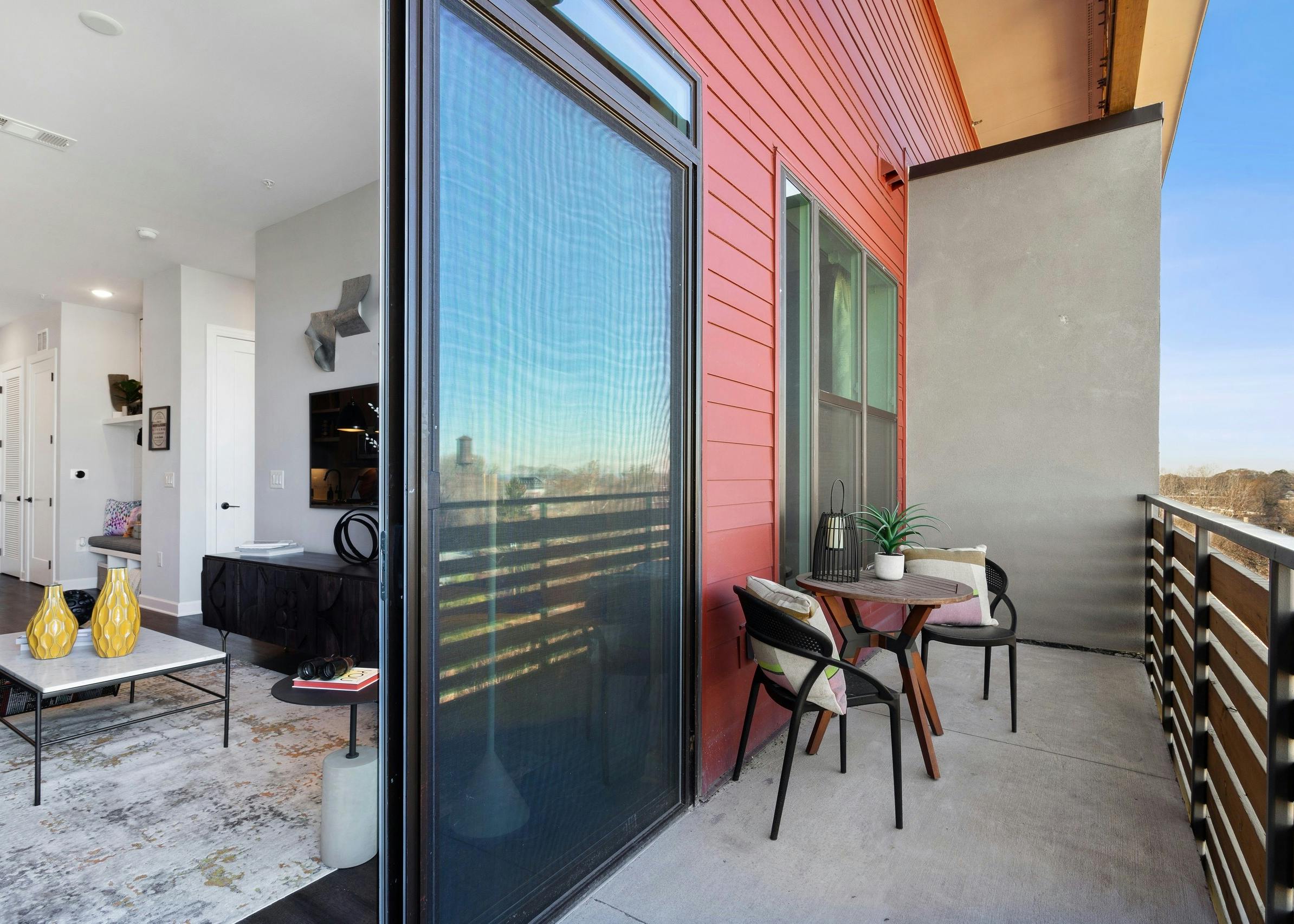 Daytime view of model apartment balcony with table and chairs and peek into living room area at AMLI Westside apartments